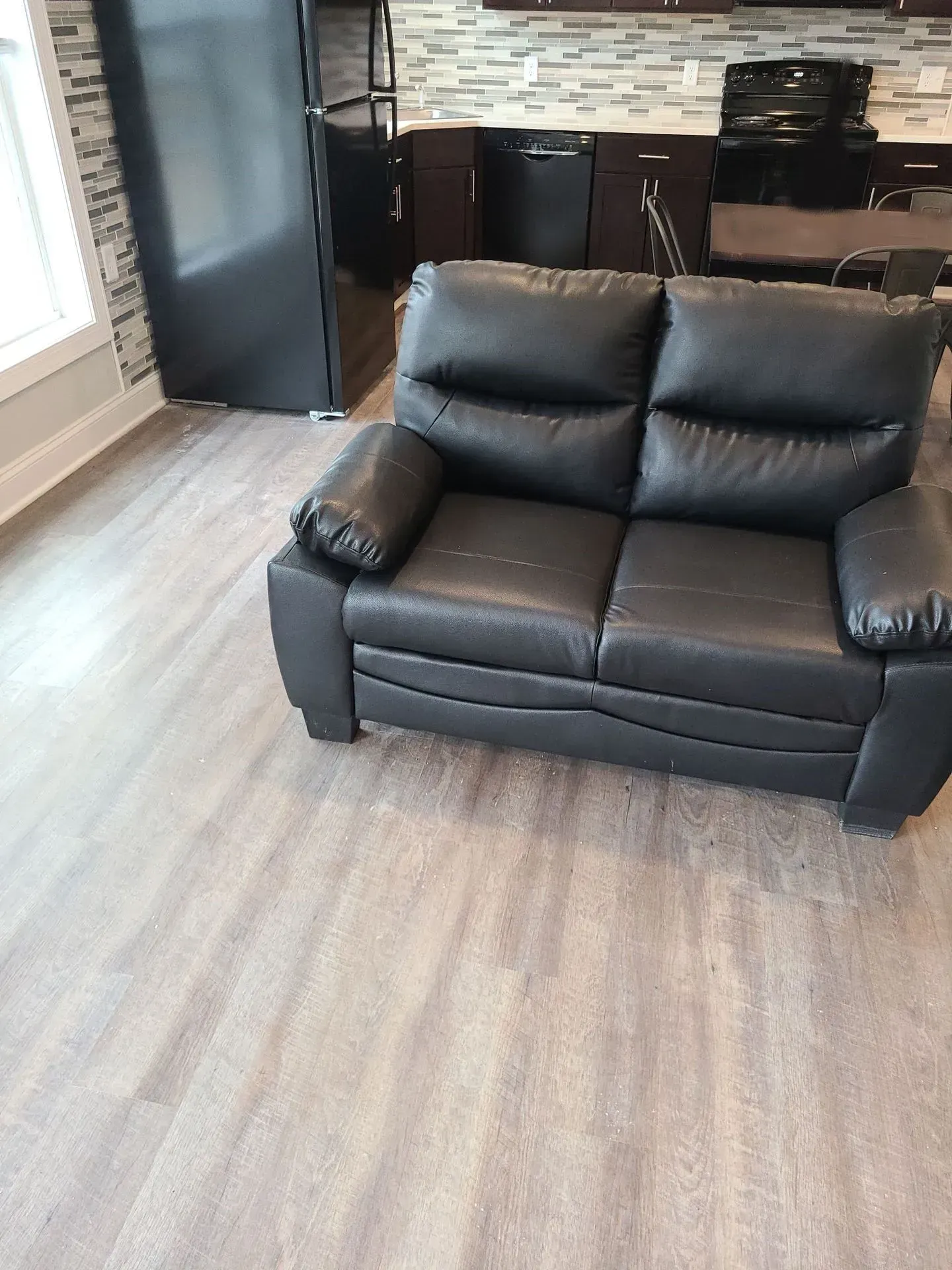 A black leather couch is sitting in a living room next to a kitchen.