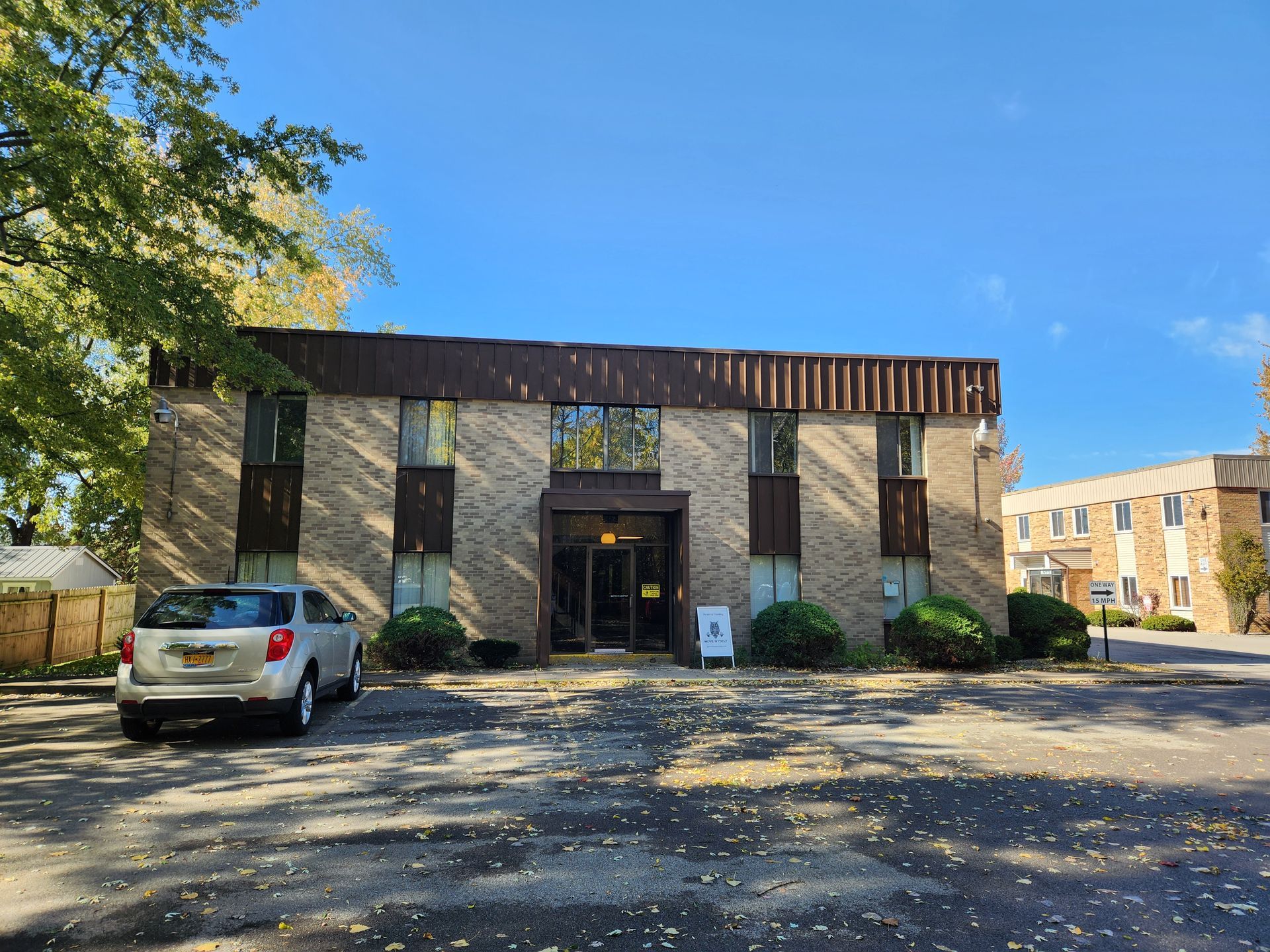 A white car is parked in front of a large brick building.