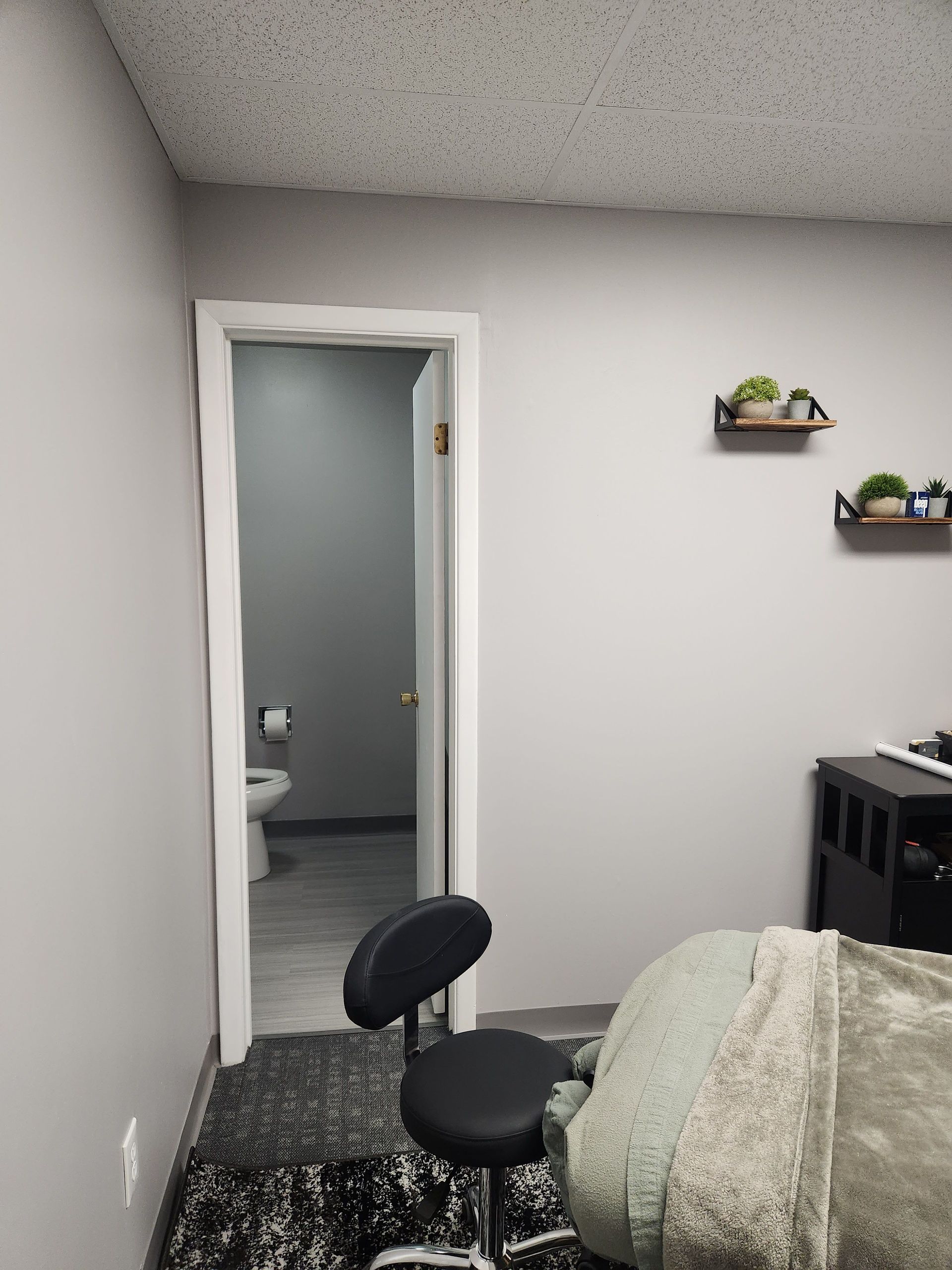 A room with a bed and a chair and a door leading to a bathroom.