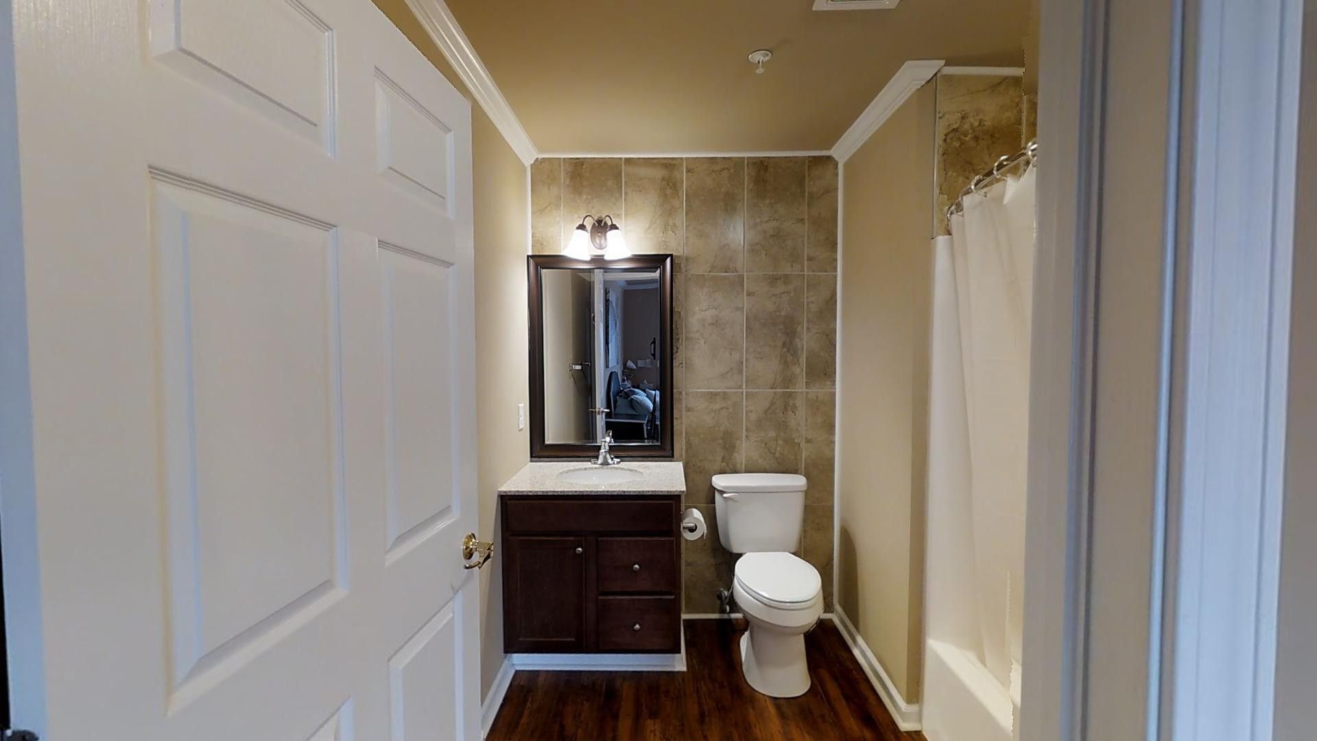 A bathroom with a toilet , sink , mirror and shower curtain.