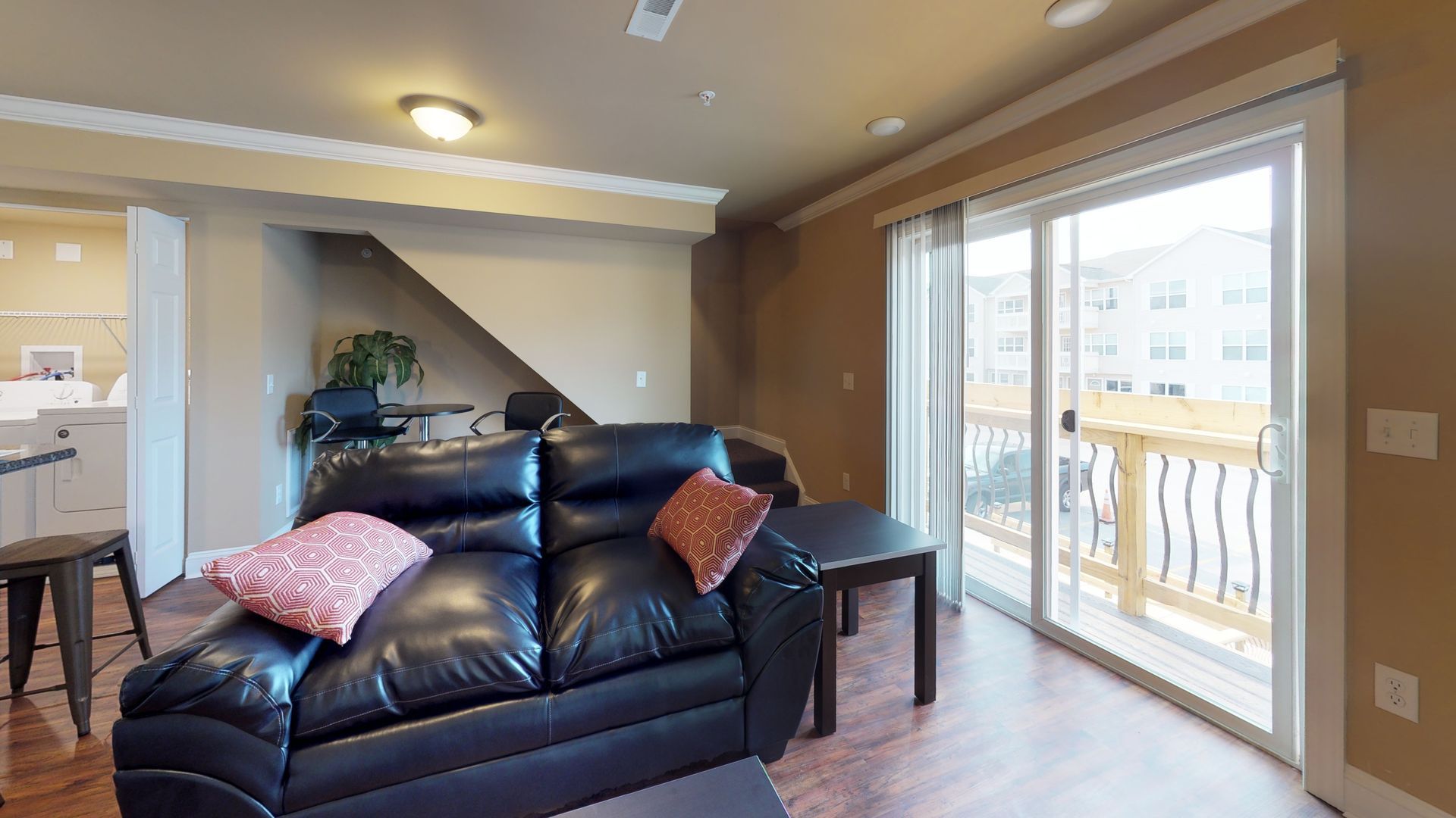 A living room with a black leather couch and sliding glass doors leading to a balcony.