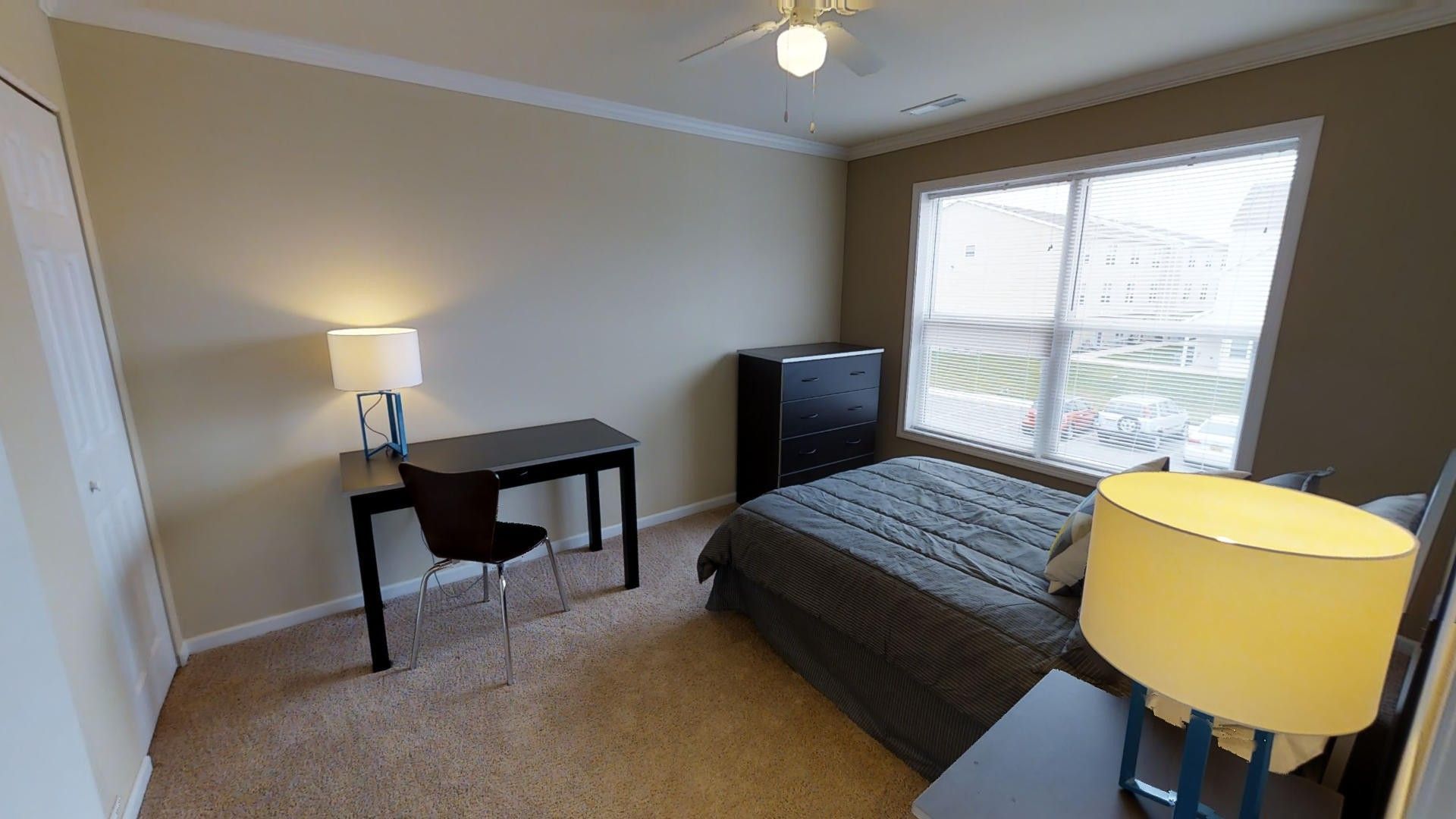A bedroom with a bed , desk , lamp and window.