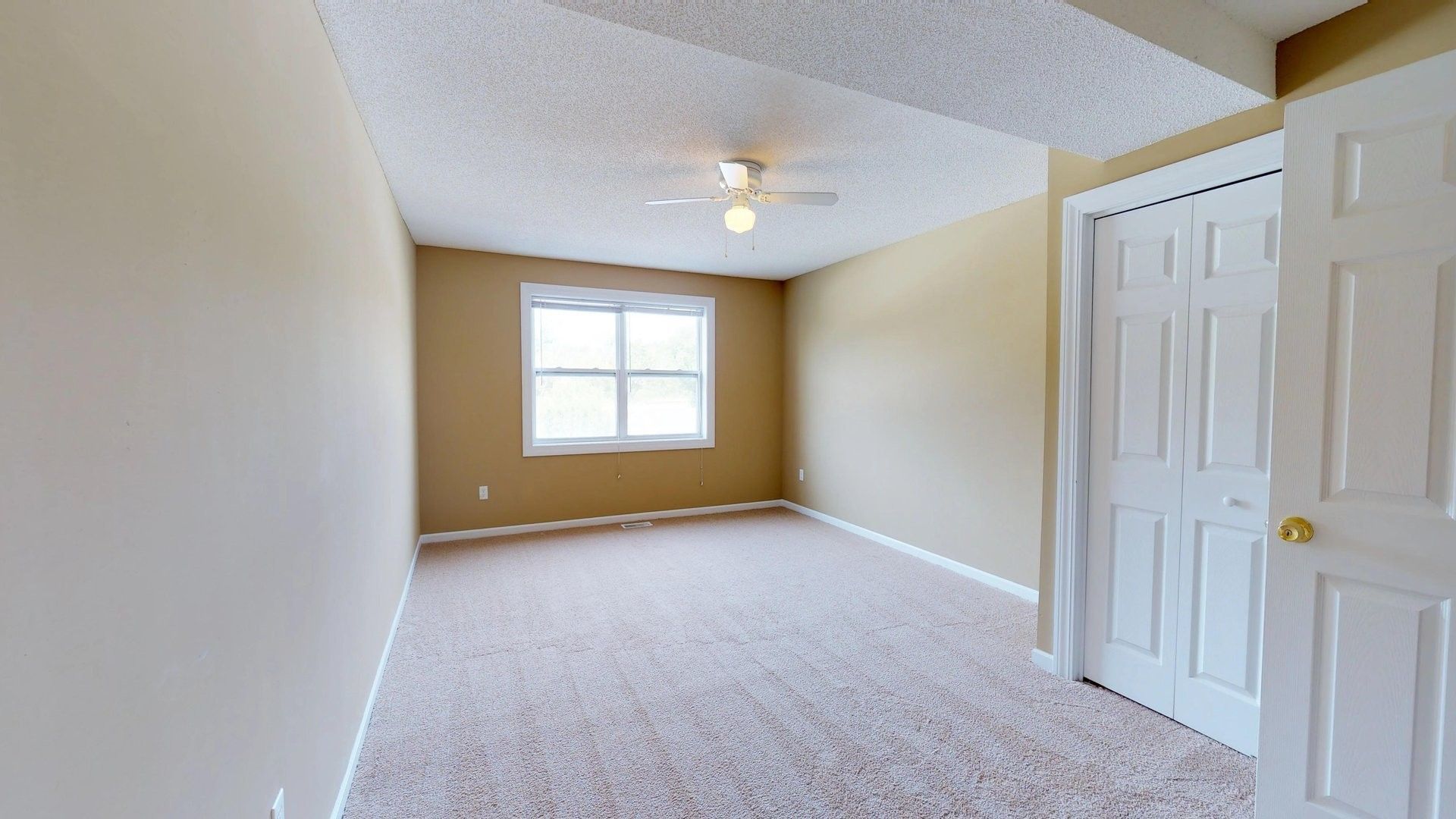 An empty bedroom with a ceiling fan and a window.