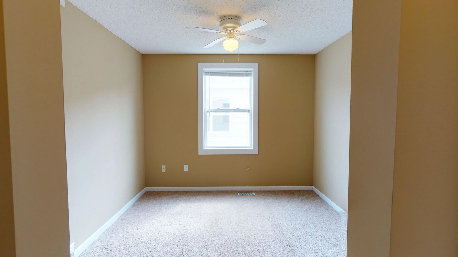 An empty bedroom with a ceiling fan and a window.
