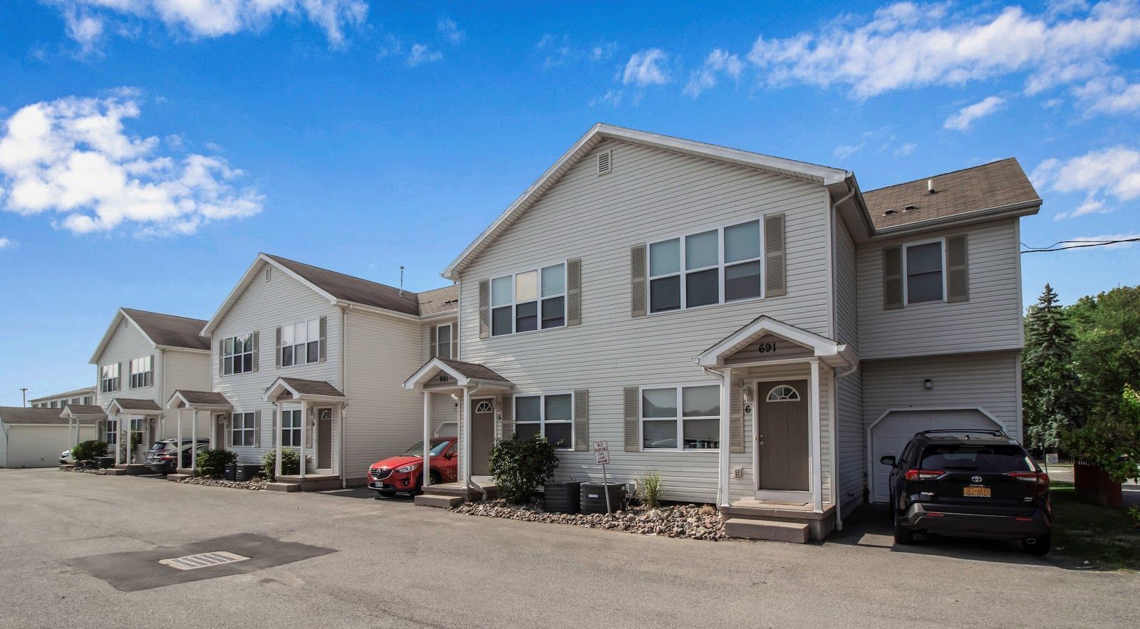 A row of white houses with cars parked in front of them.