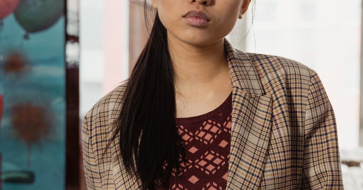 A woman wearing a plaid jacket and a ponytail is standing in front of a window.