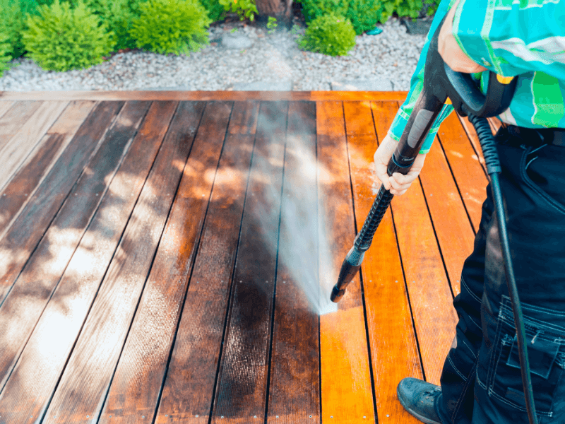 Person pressure washing a wooden deck, cleaning the dark stained wood.