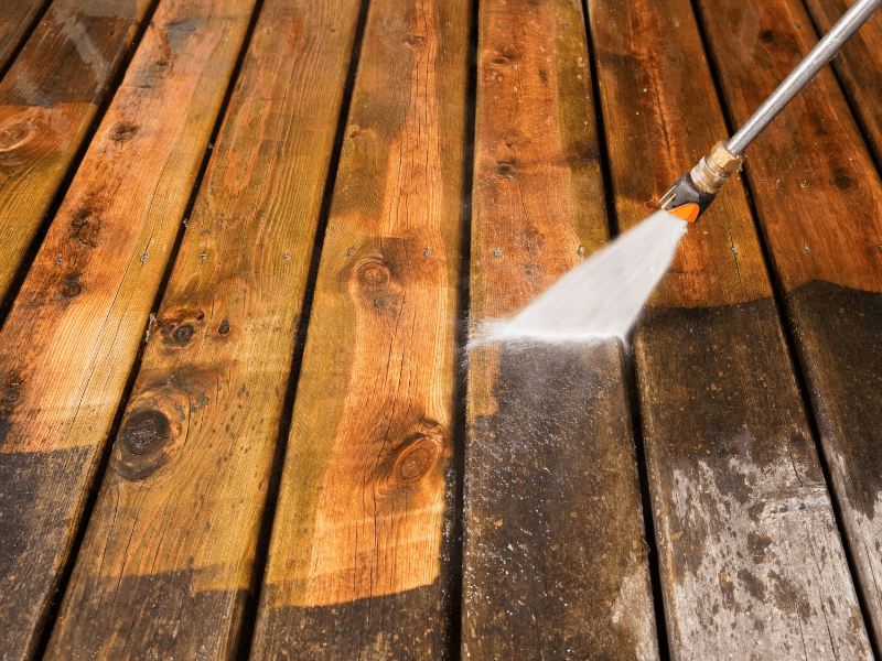 A power washer cleaning a wooden deck, revealing lighter wood.