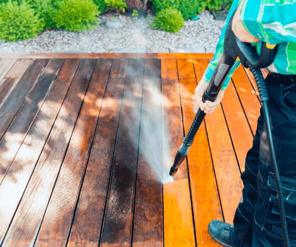 Person pressure washing a wooden deck, cleaning the dark stained wood.