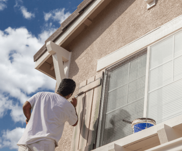 Man painting exterior trim of a house with a blue sky background.