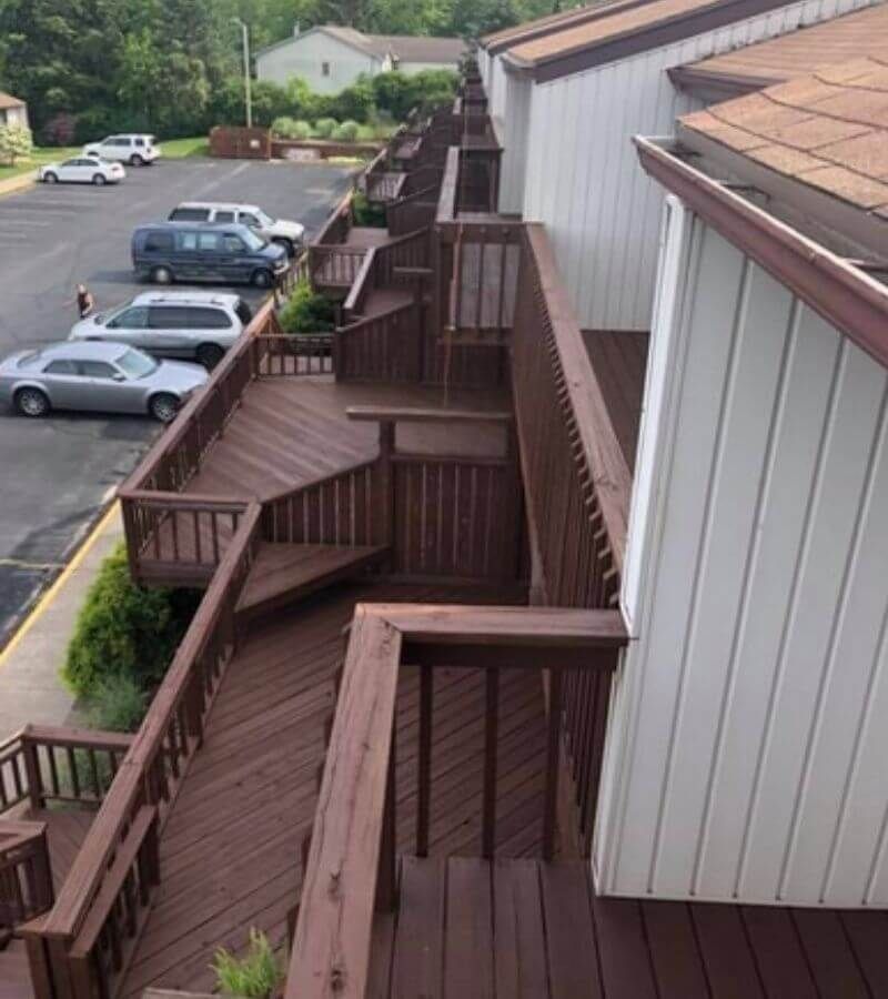 Brown wooden stairs and decks leading to apartments with cars parked below.