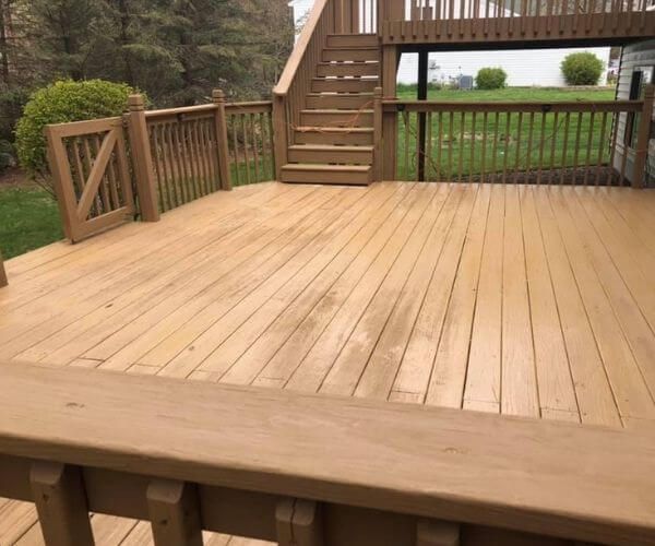 Wooden deck with stairs, railing, and a small gate. Brown wood, set outdoors with green grass visible.