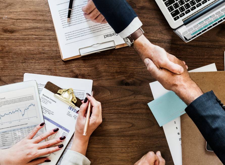 Hombres de negocios se dan la mano para firmar un contrato sobre una mesa de madera.