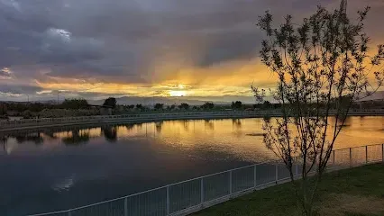 A sunset over a lake with a fence and trees in the foreground.