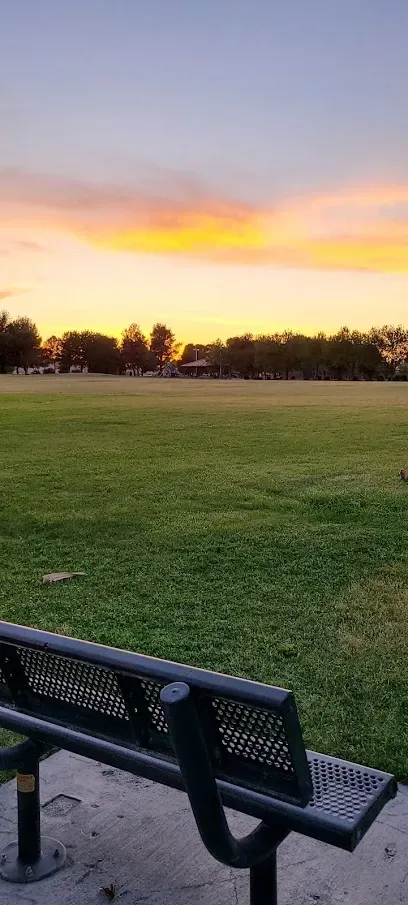 A park bench with a view of a field at sunset.