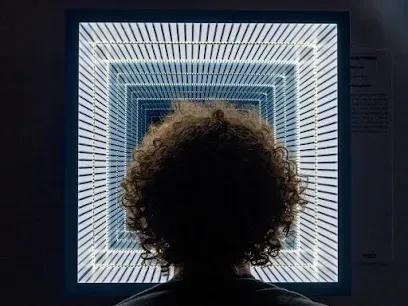 A man with curly hair is looking at an optical illusion on a screen.