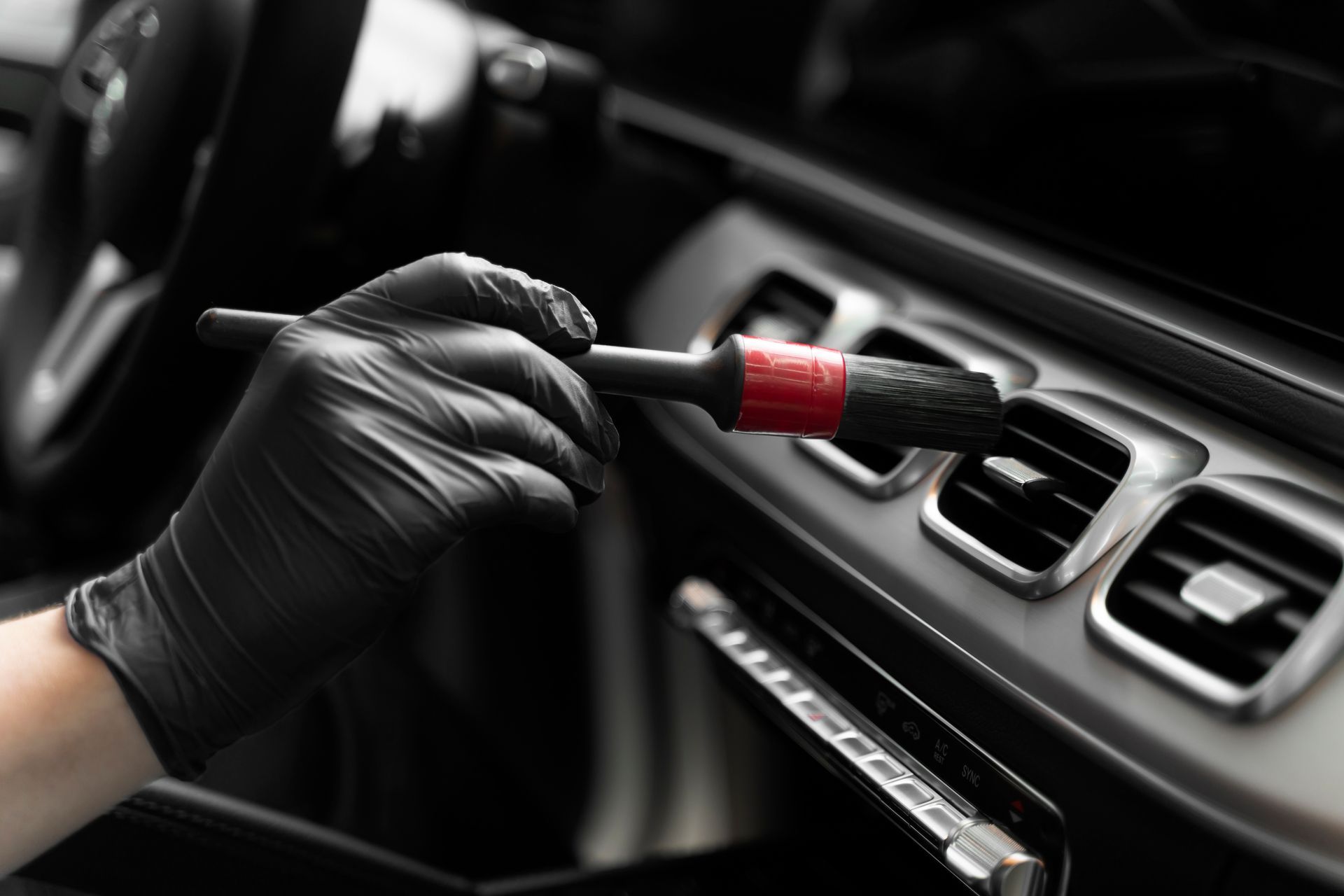 a person wearing black gloves is cleaning the air vents of a car with a brush .
