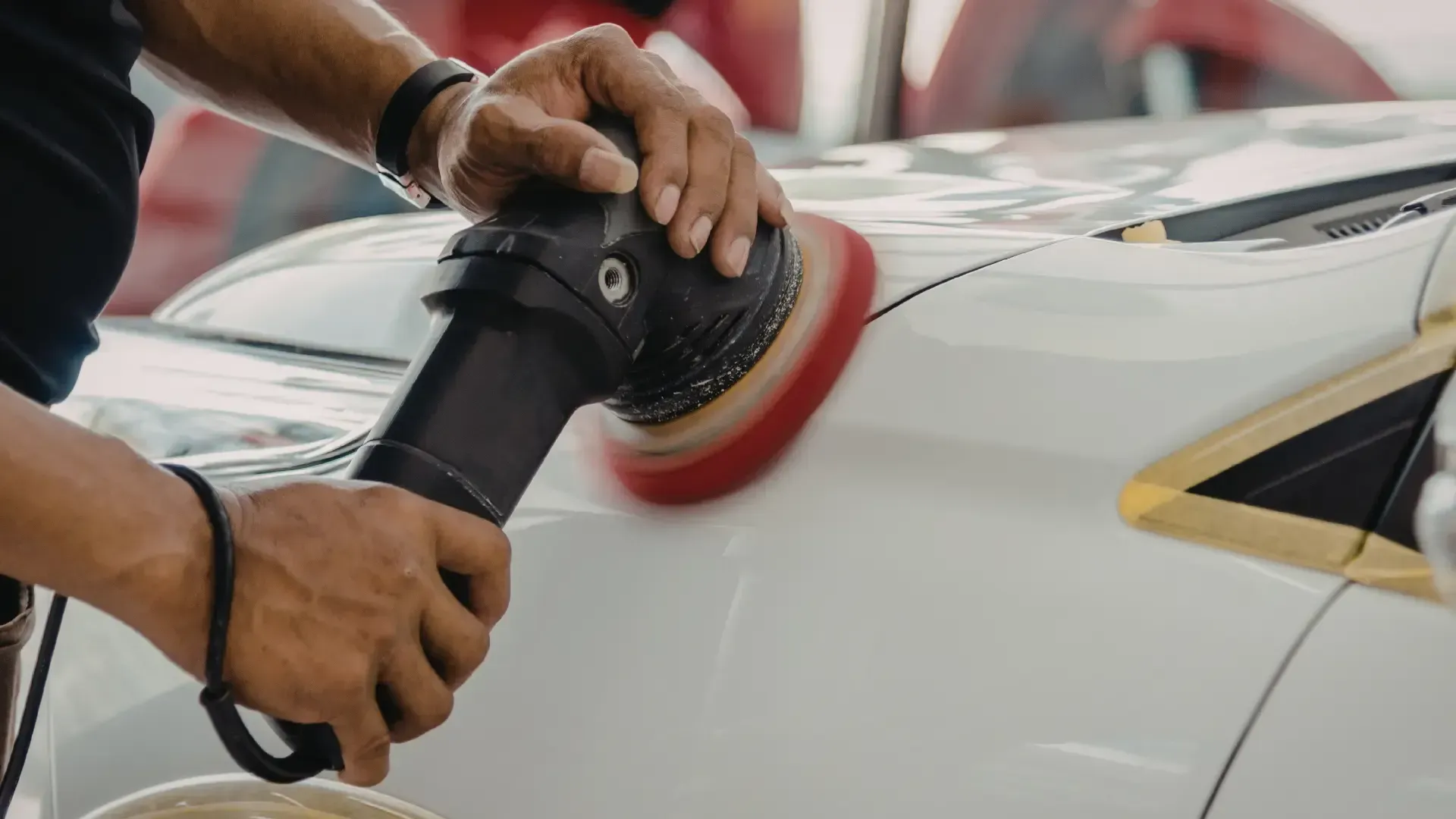 Person using an orbital buffer on a white car to polish the paint.