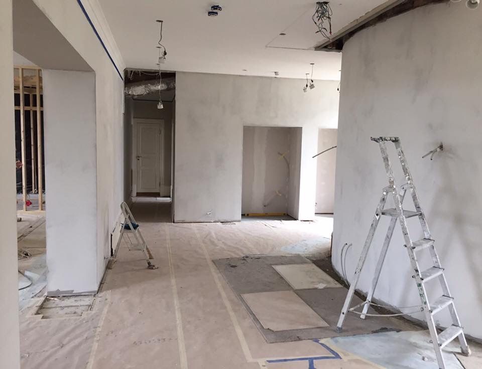 Før-bilde. Interiør under renovering med synlige ledninger, uferdige vegger og stige.