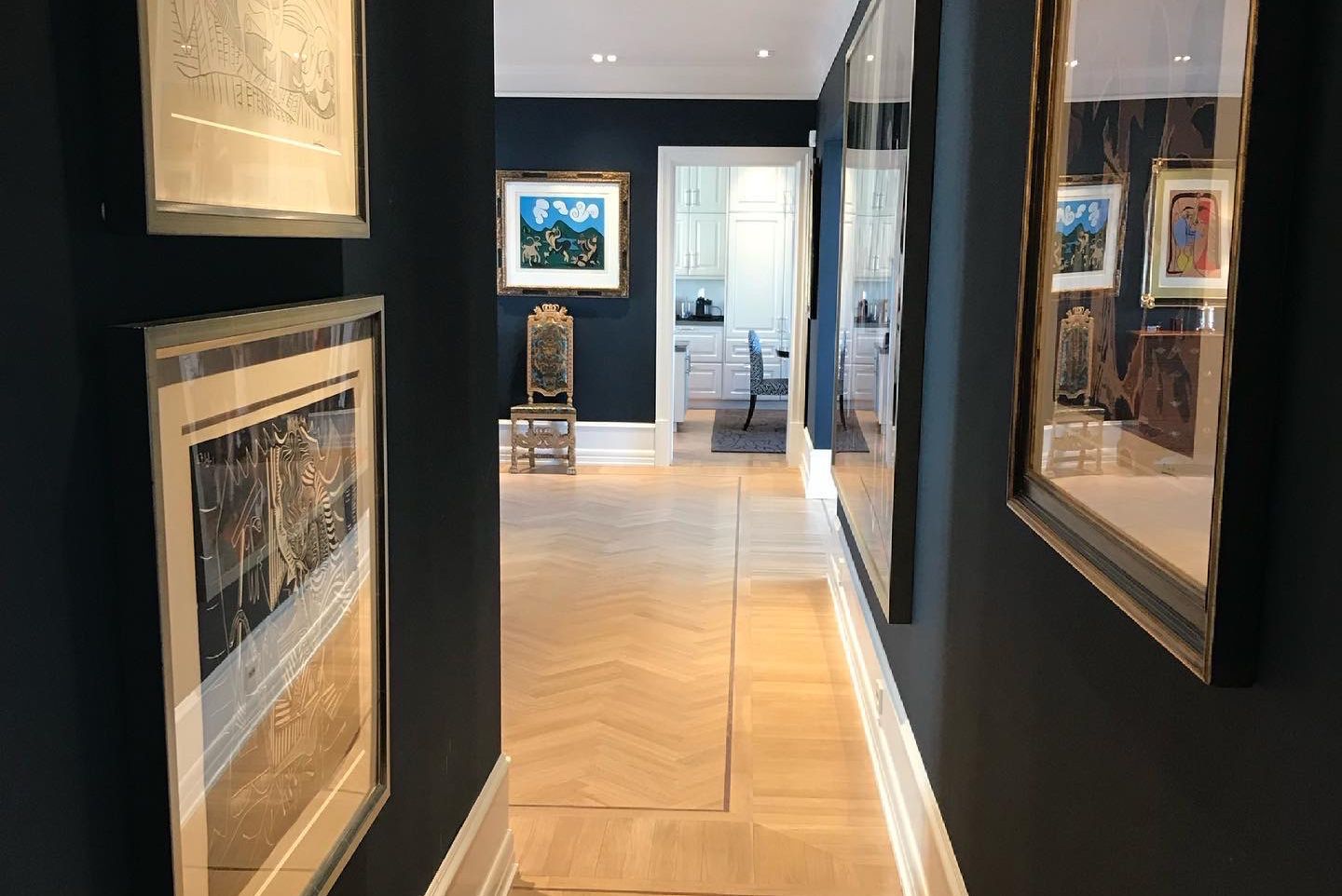 Smal gang med mørkeblå vegger, kunst og lyst fiskebensgulv.