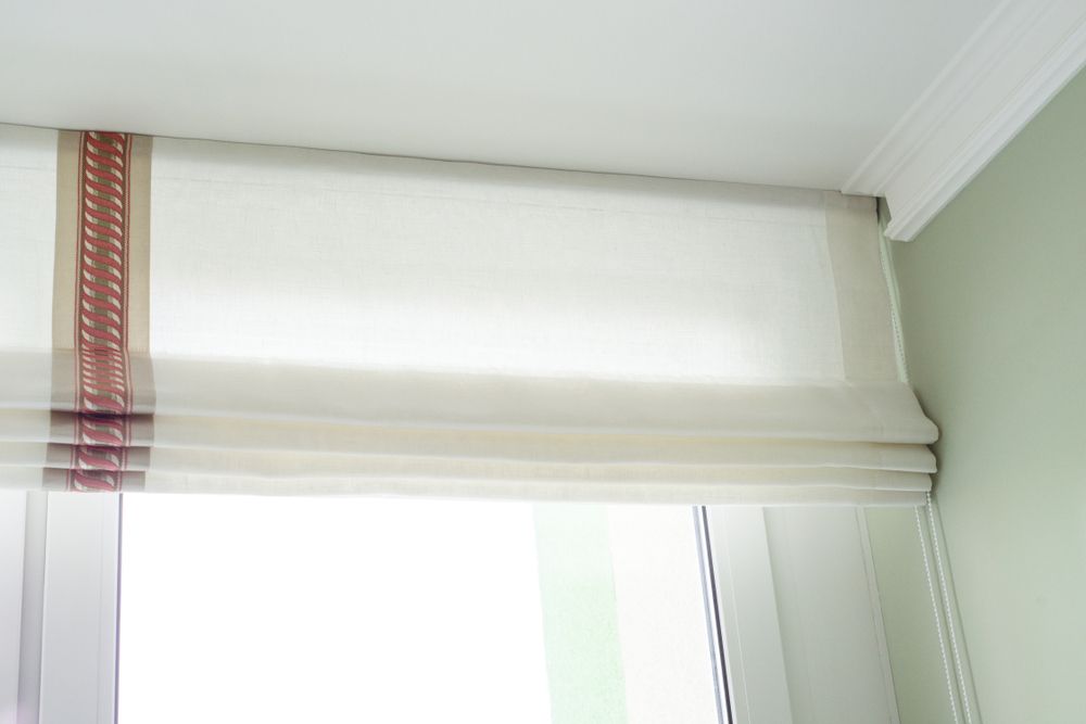 A White Roman Shade Is Hanging Over A Window In A Room — Caba's Drapery In Coffs Harbour, NSW