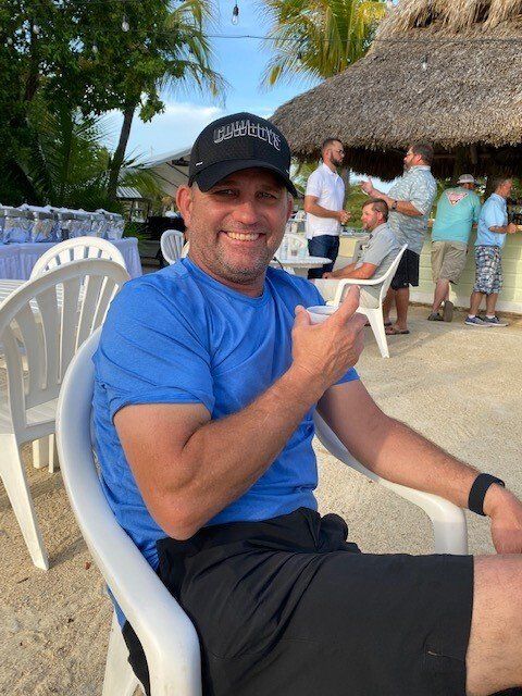 A man in a blue shirt and black hat is sitting in a white chair