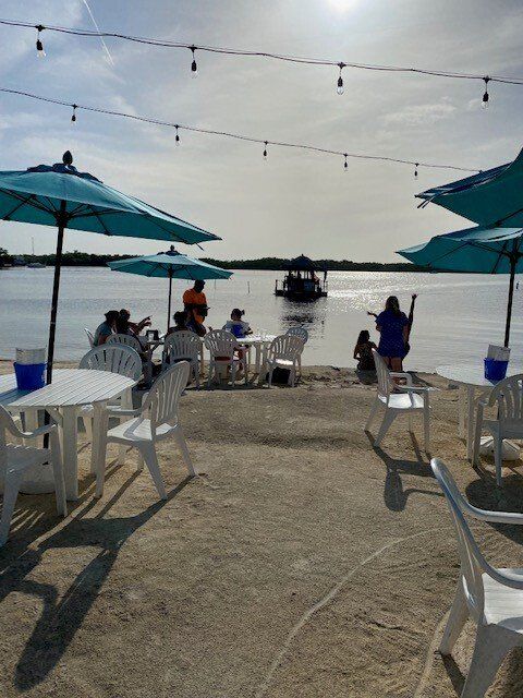 A group of people sit at tables under umbrellas on a beach