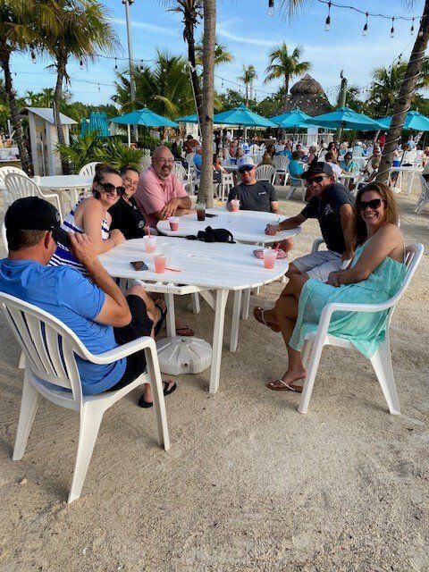 A group of people are sitting around a table on the beach
