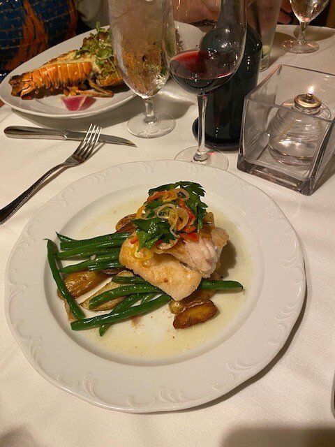 A white plate topped with a piece of fish and green beans on a table.