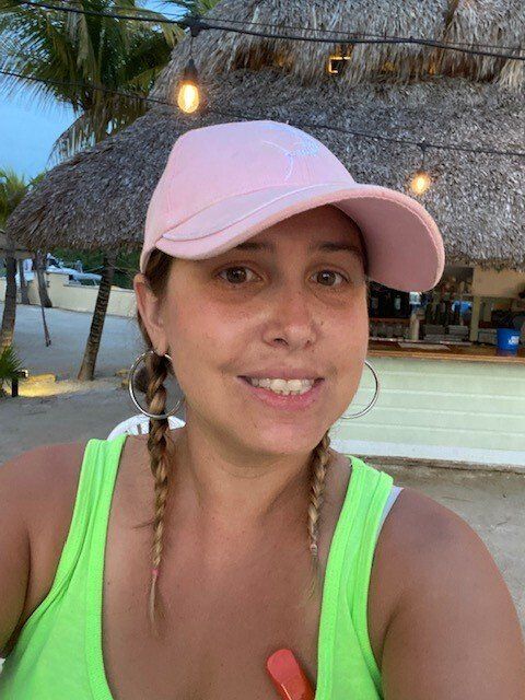 A woman wearing a pink hat and a green tank top is taking a selfie.