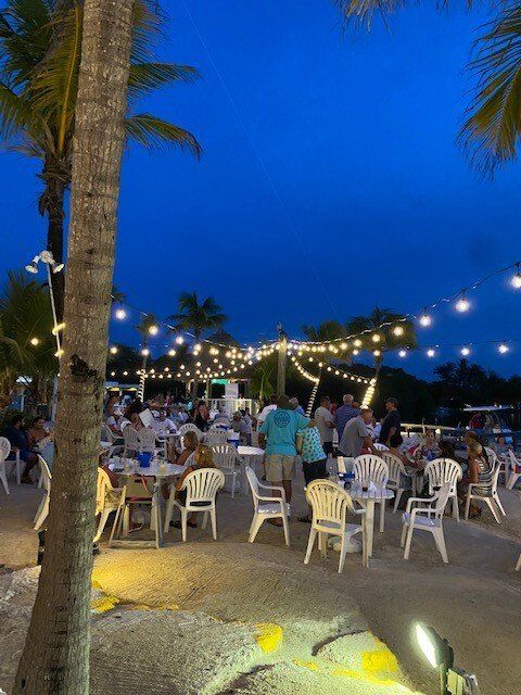 A group of people are sitting at tables and chairs on a beach at night.