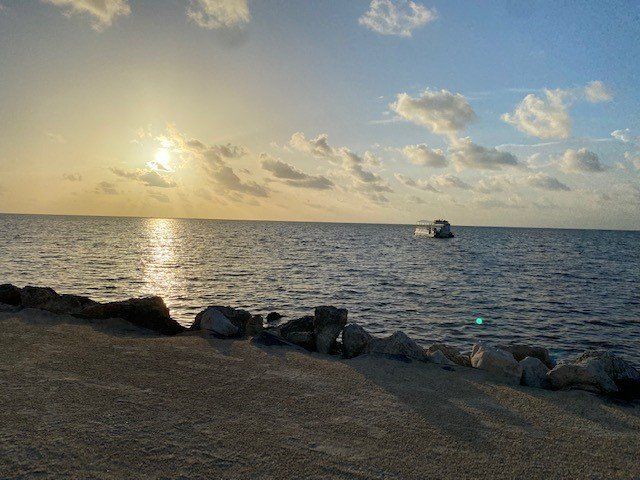 The sun is setting over the ocean with a boat in the distance.