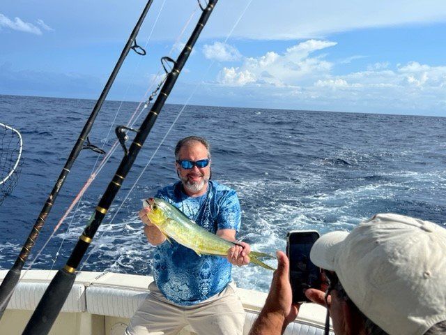A man is holding a fish on a boat while another man takes a picture.