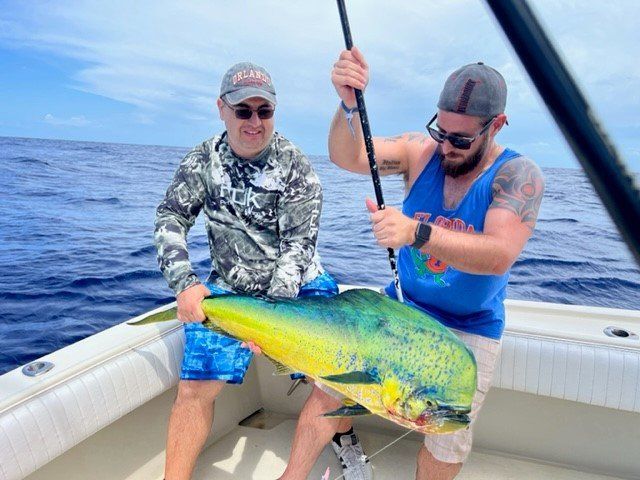 Two men are sitting on a boat holding a large fish.