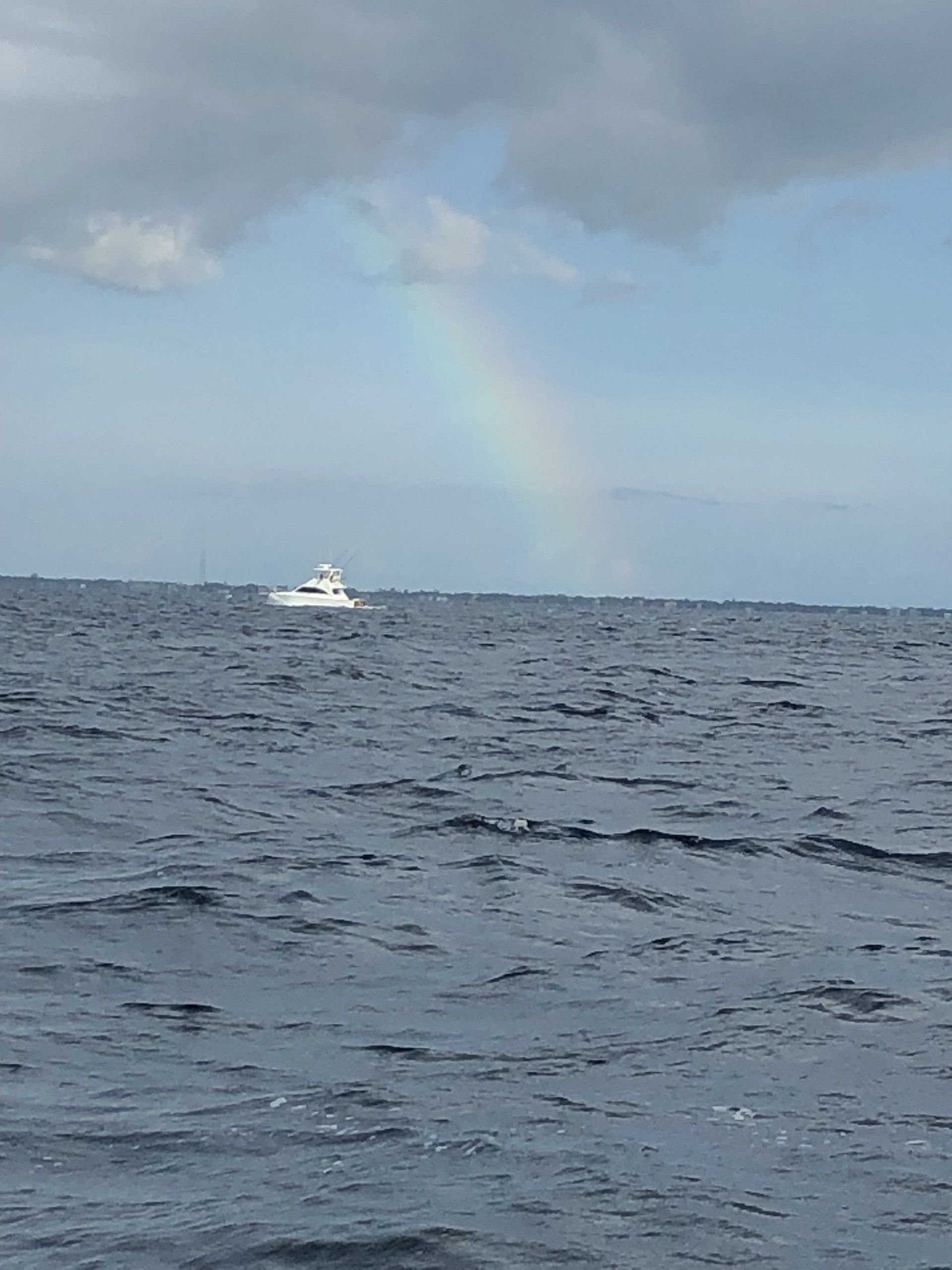 A boat is floating on top of a large body of water with a rainbow in the sky.