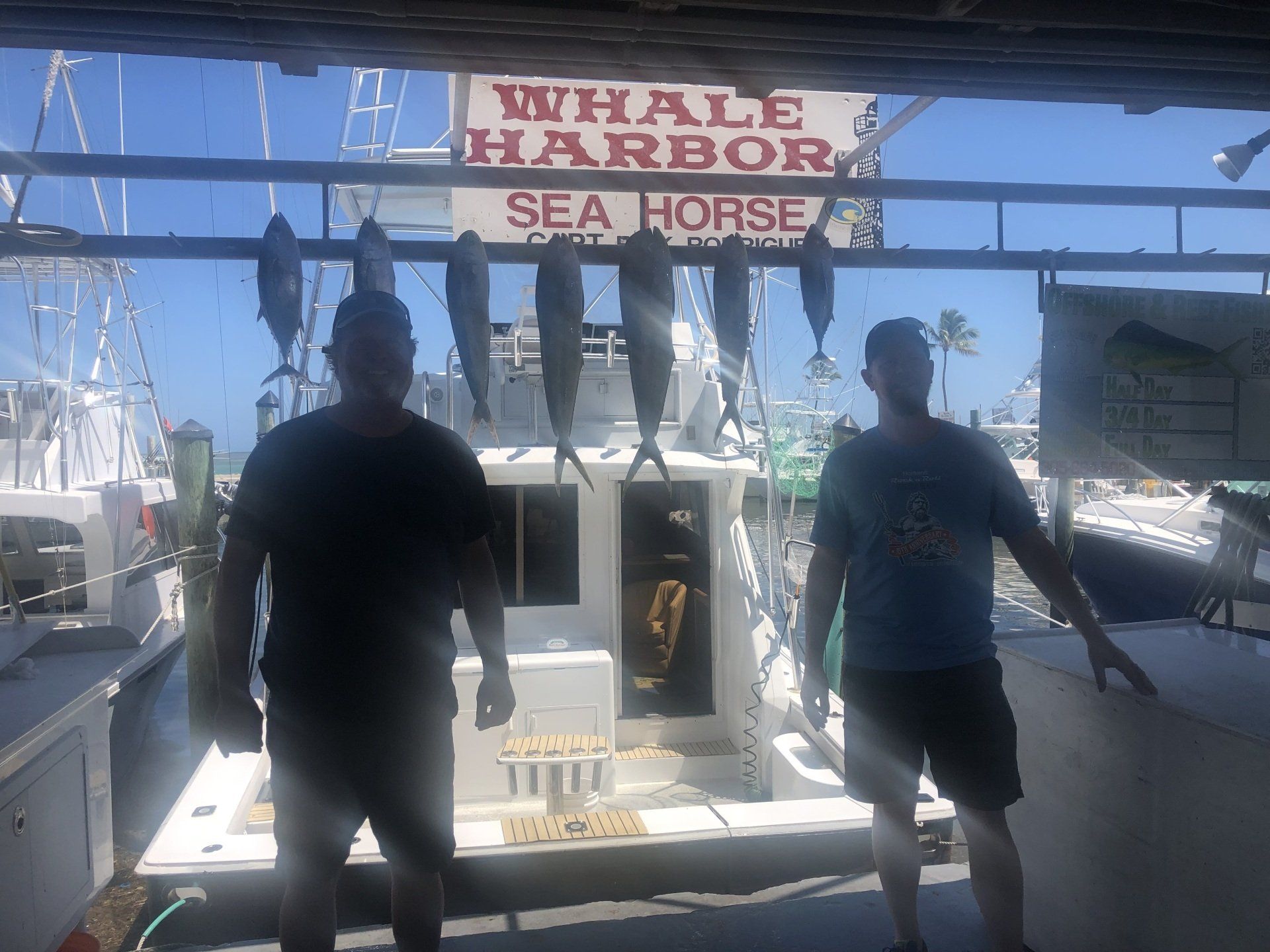 Two men are standing in front of a boat that says whale harbor sea horse