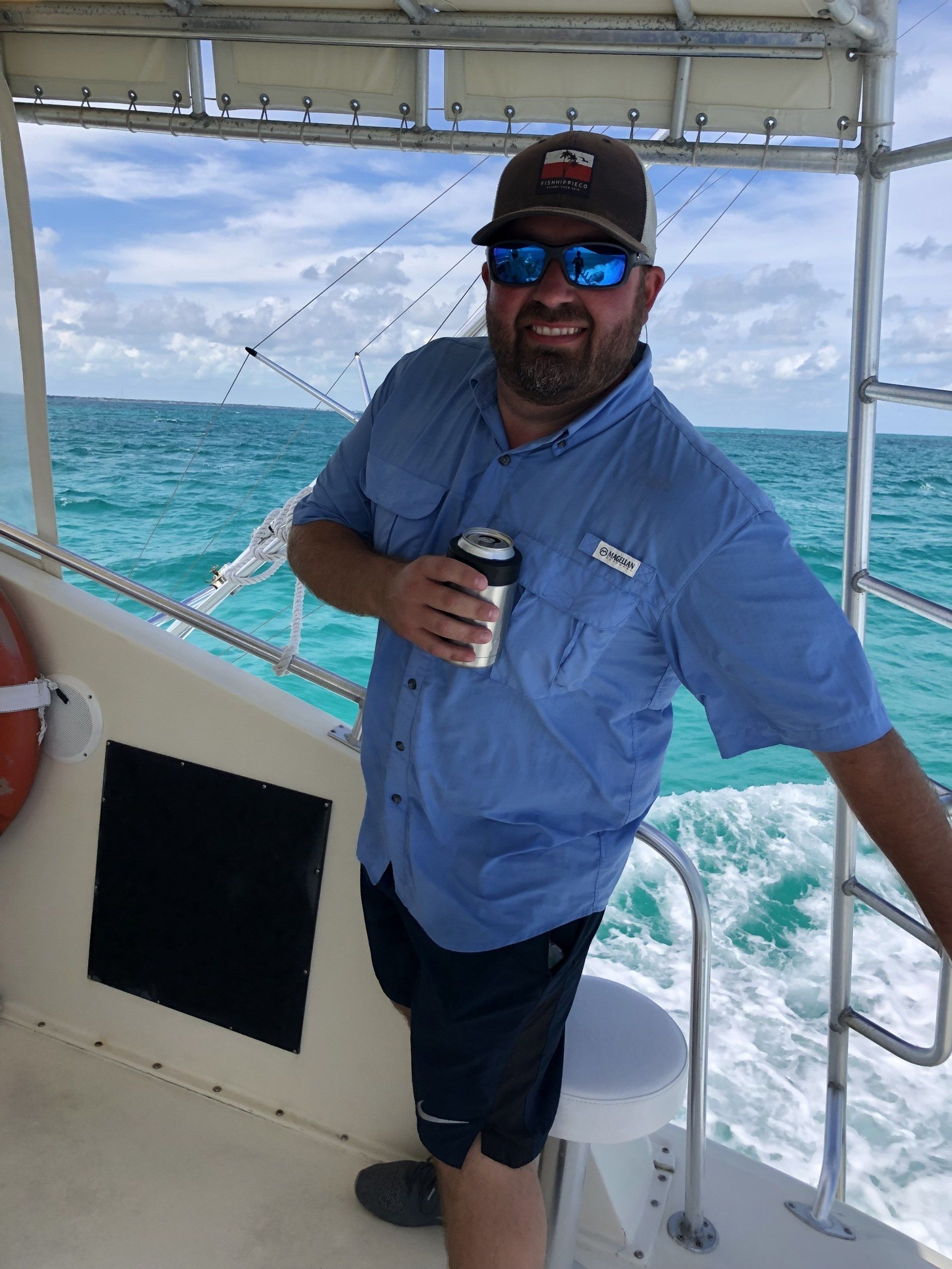 A man is standing on the deck of a boat holding a can of beer.