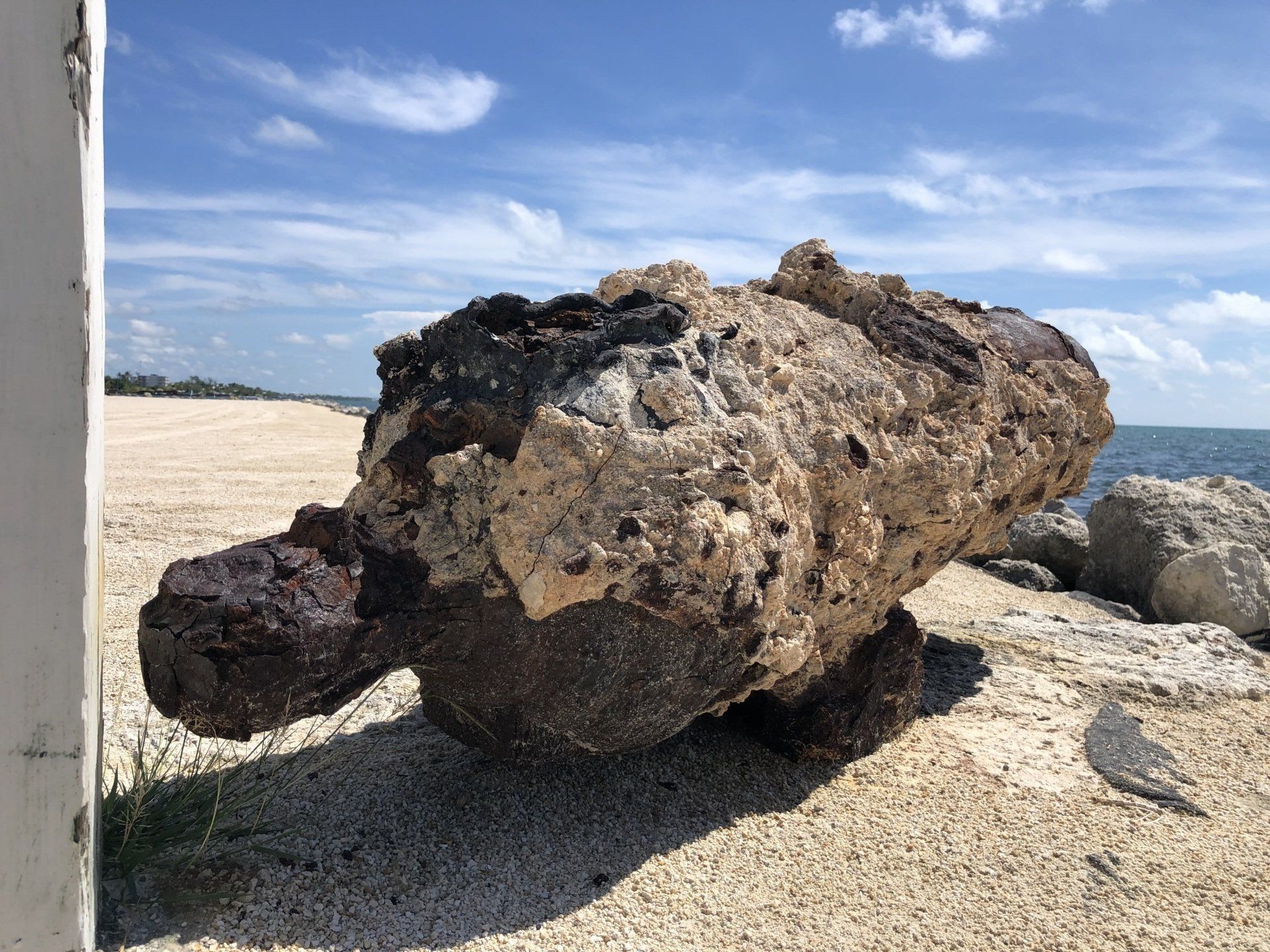 A large rock is sitting on the beach next to the ocean.