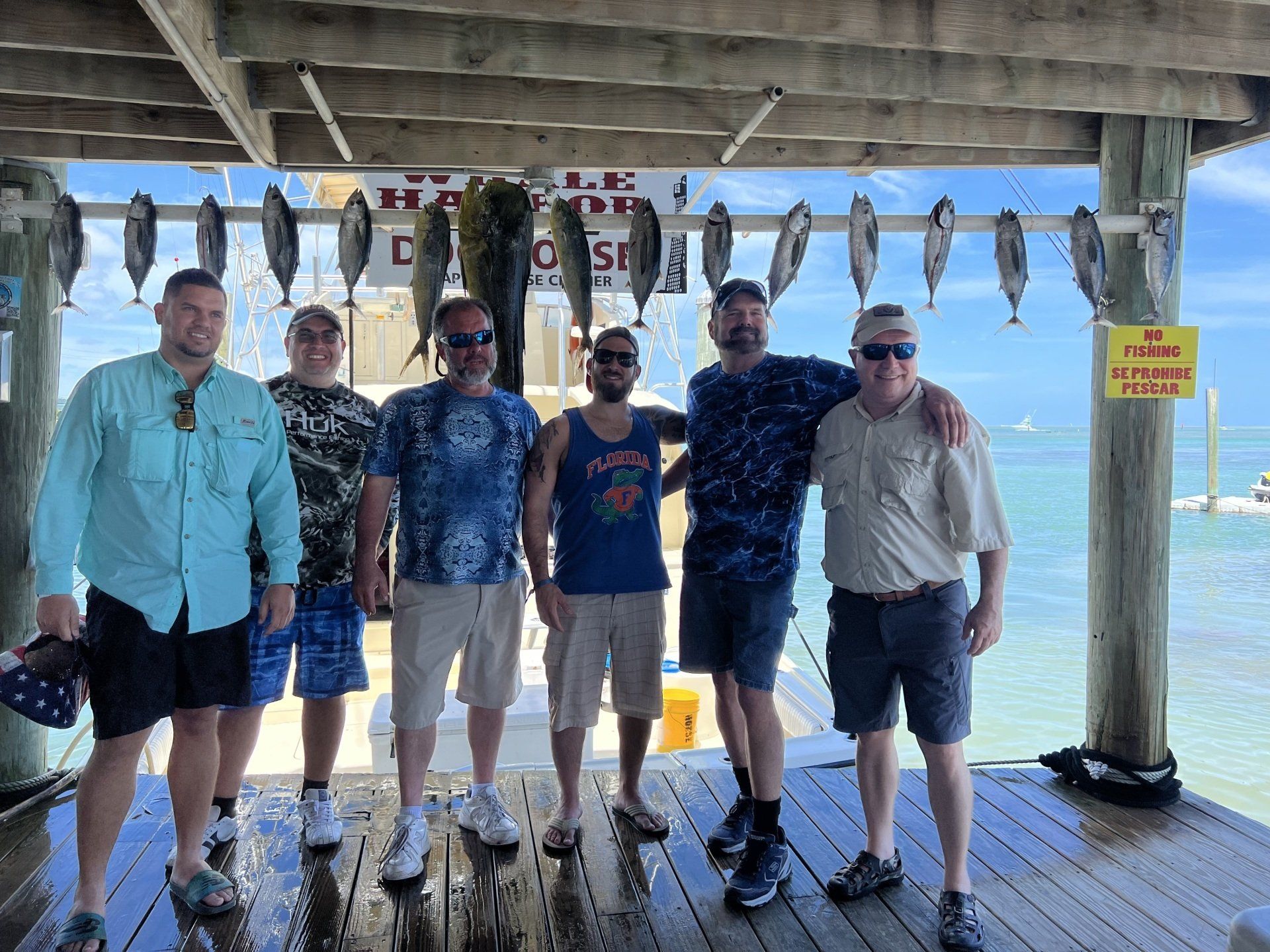 A group of men are posing for a picture on a dock with fish hanging from the ceiling.