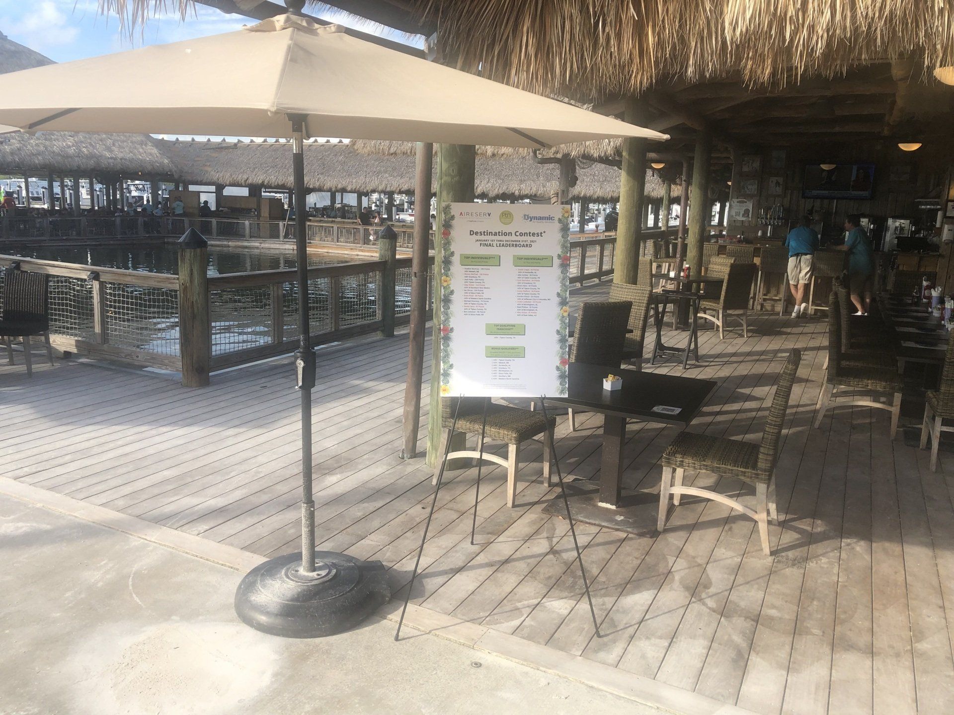 A white umbrella is sitting on a wooden deck next to a table and chairs.