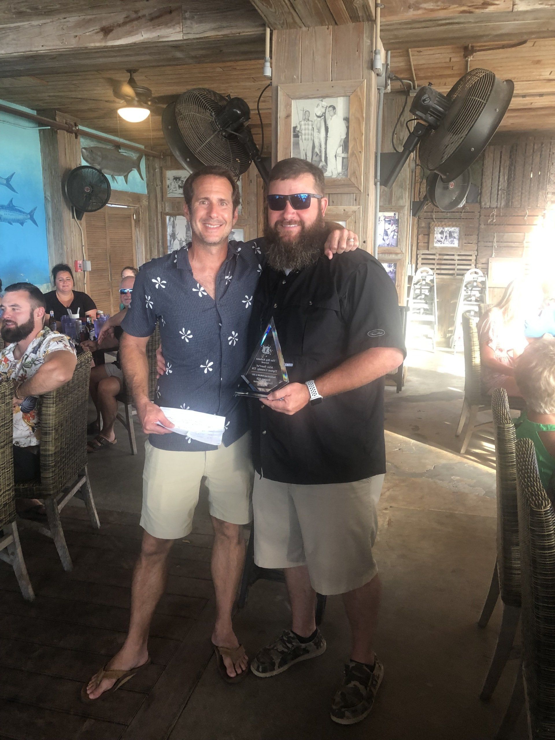 Two men are standing next to each other in a restaurant holding a trophy.