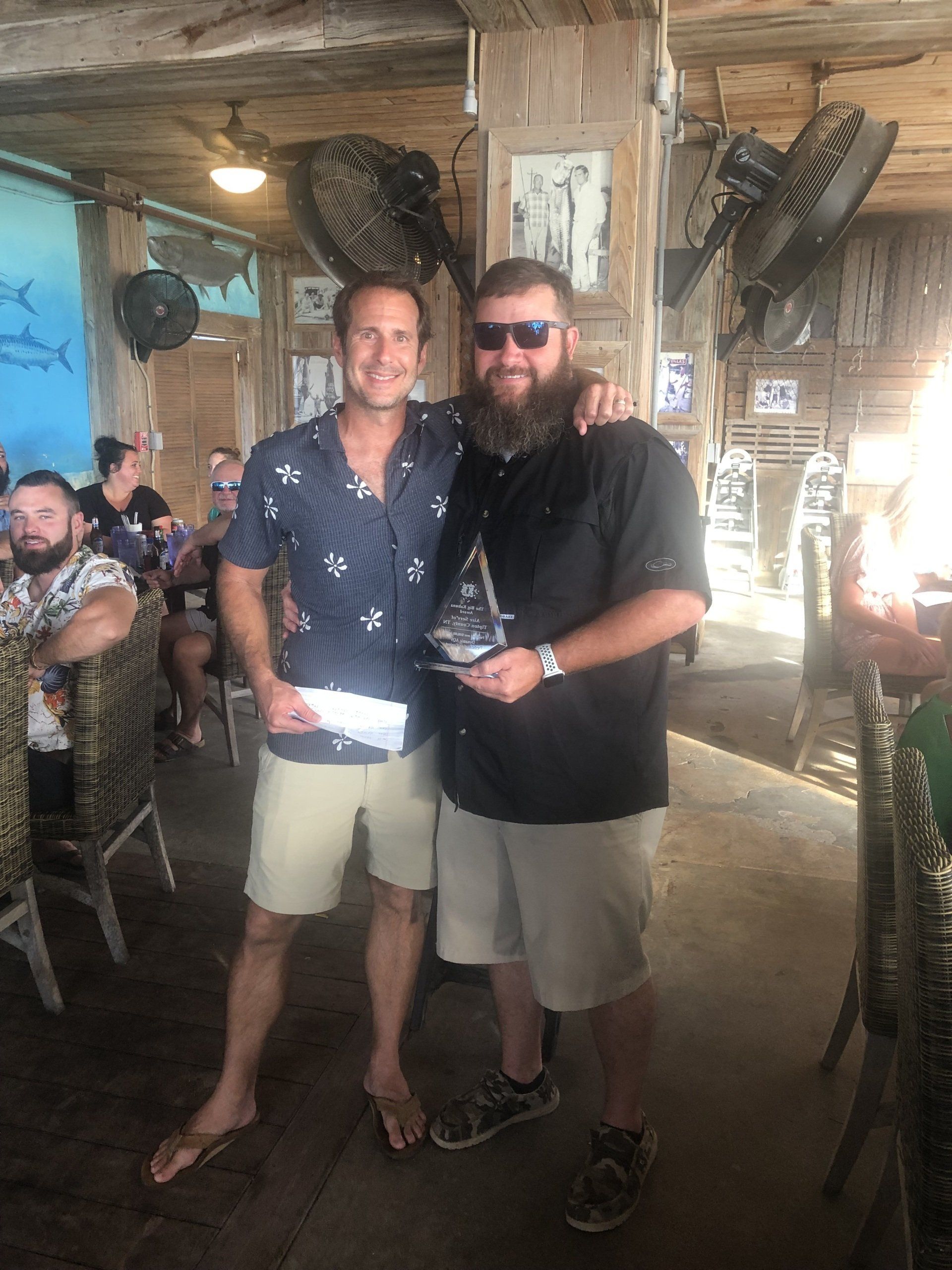 Two men are standing next to each other in a restaurant holding a trophy.