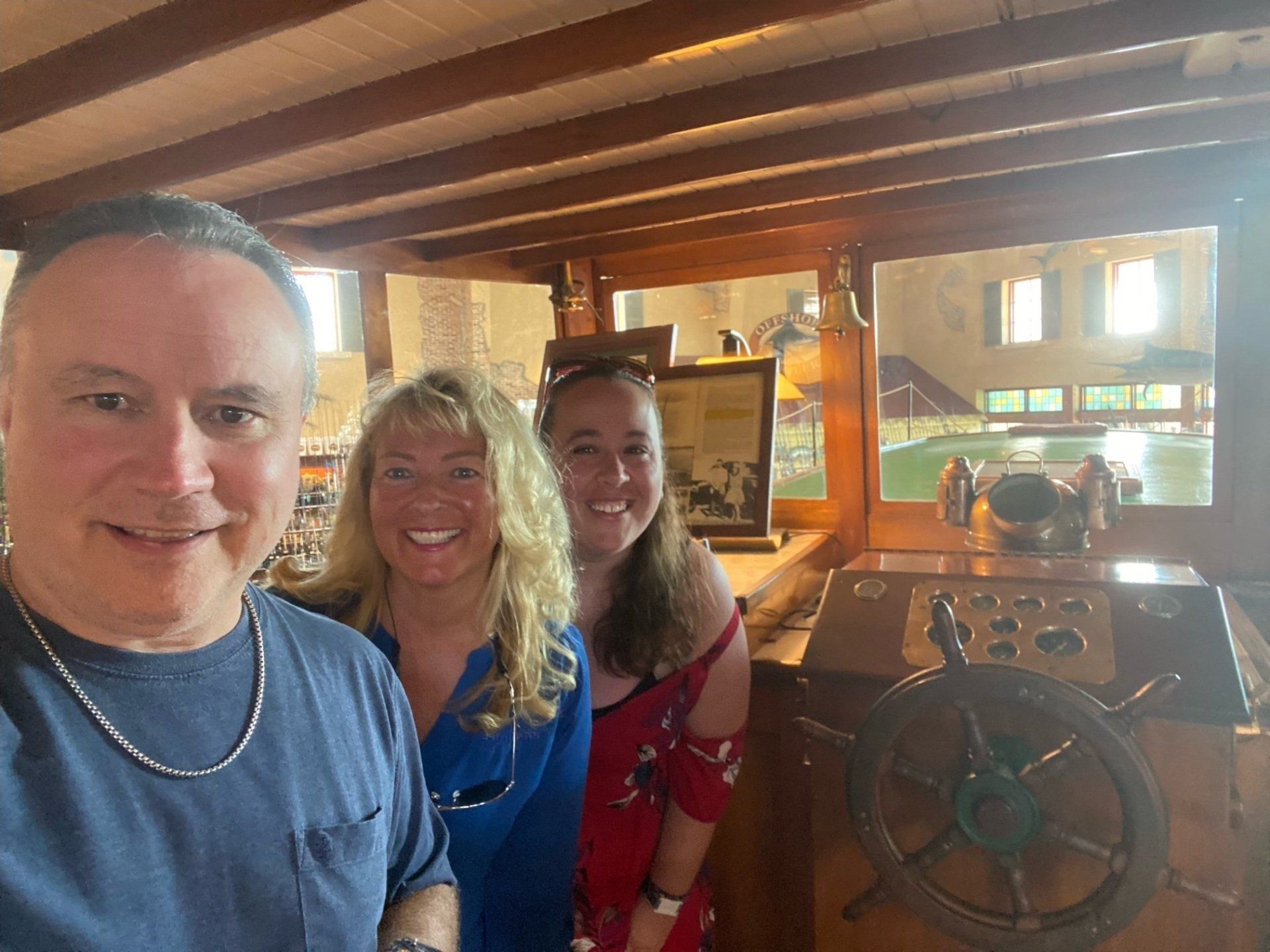 A man and two women are posing for a picture in front of a boat steering wheel.