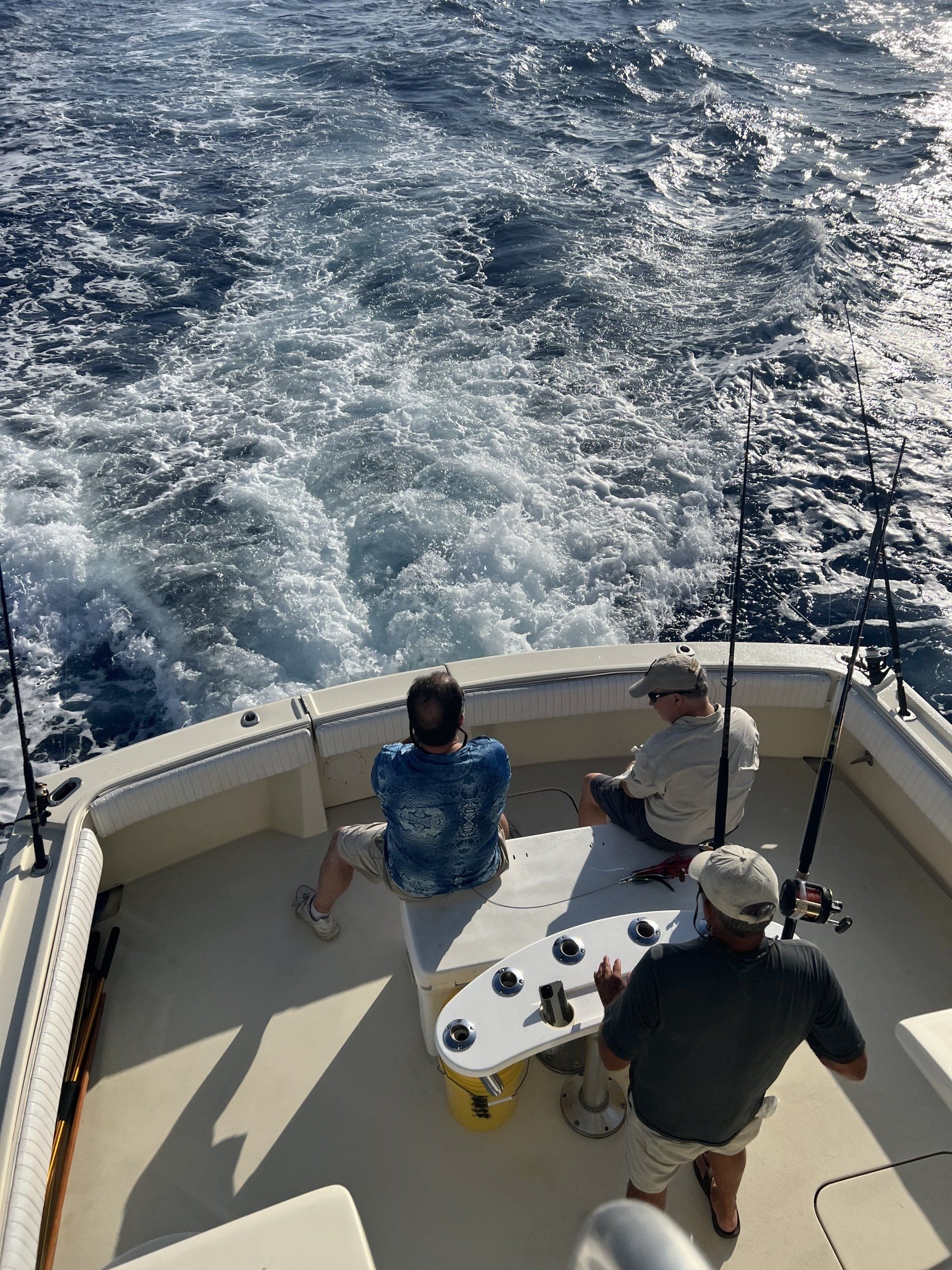 Three men are fishing on a boat in the ocean.