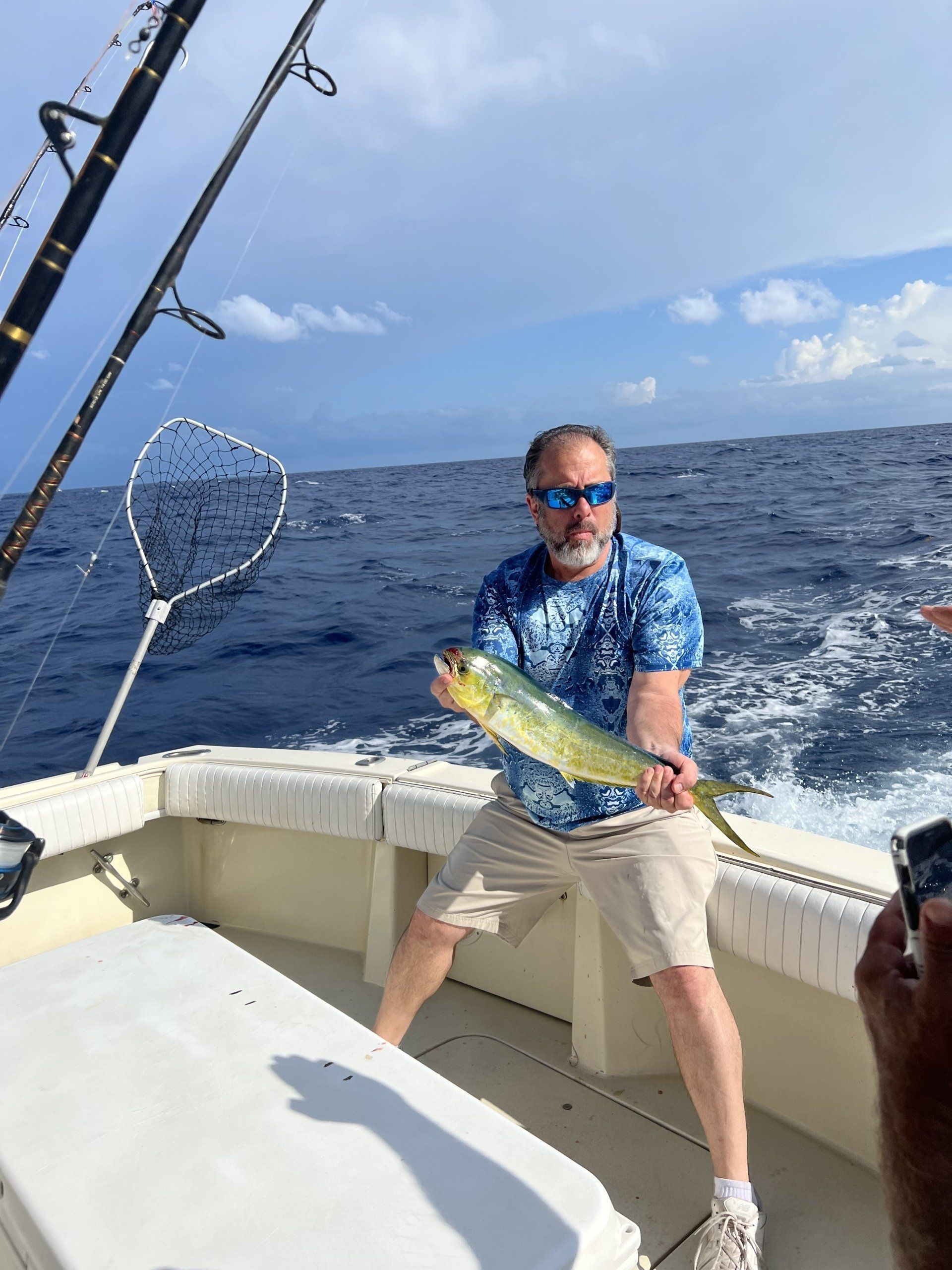 A man is holding a fish on a boat in the ocean.