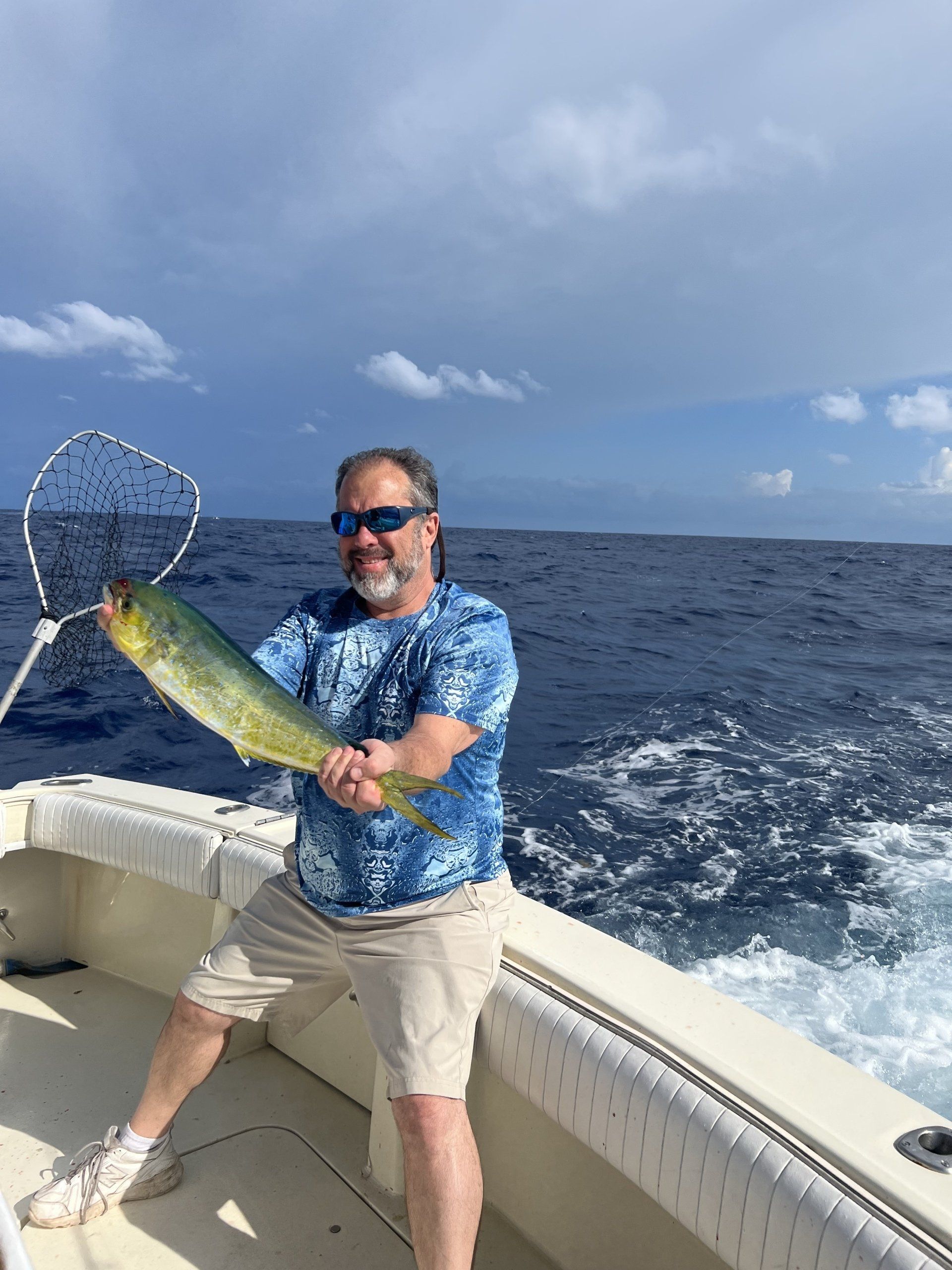 A man is holding a fish on a boat in the ocean.