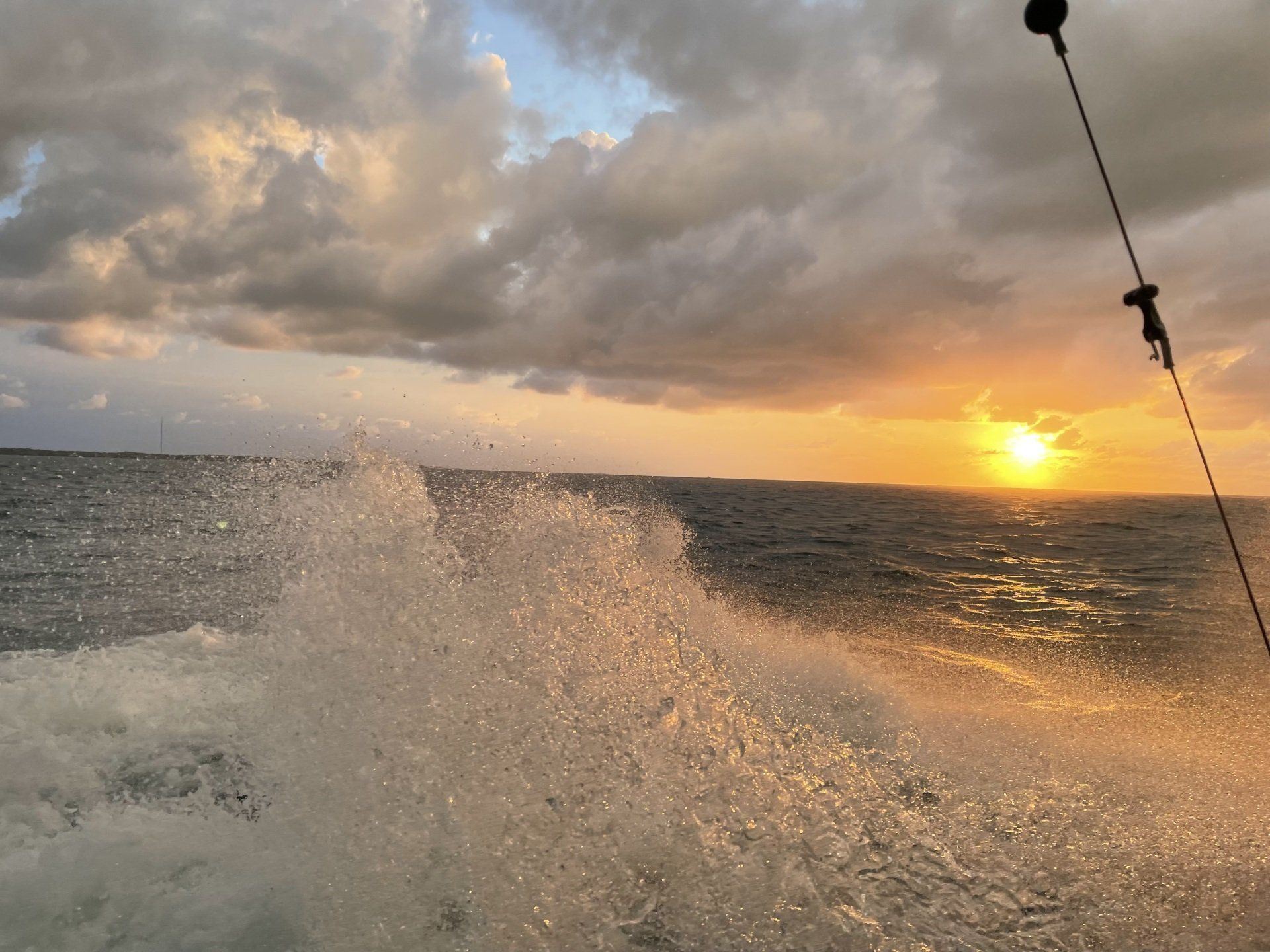 A boat is going through the ocean at sunset