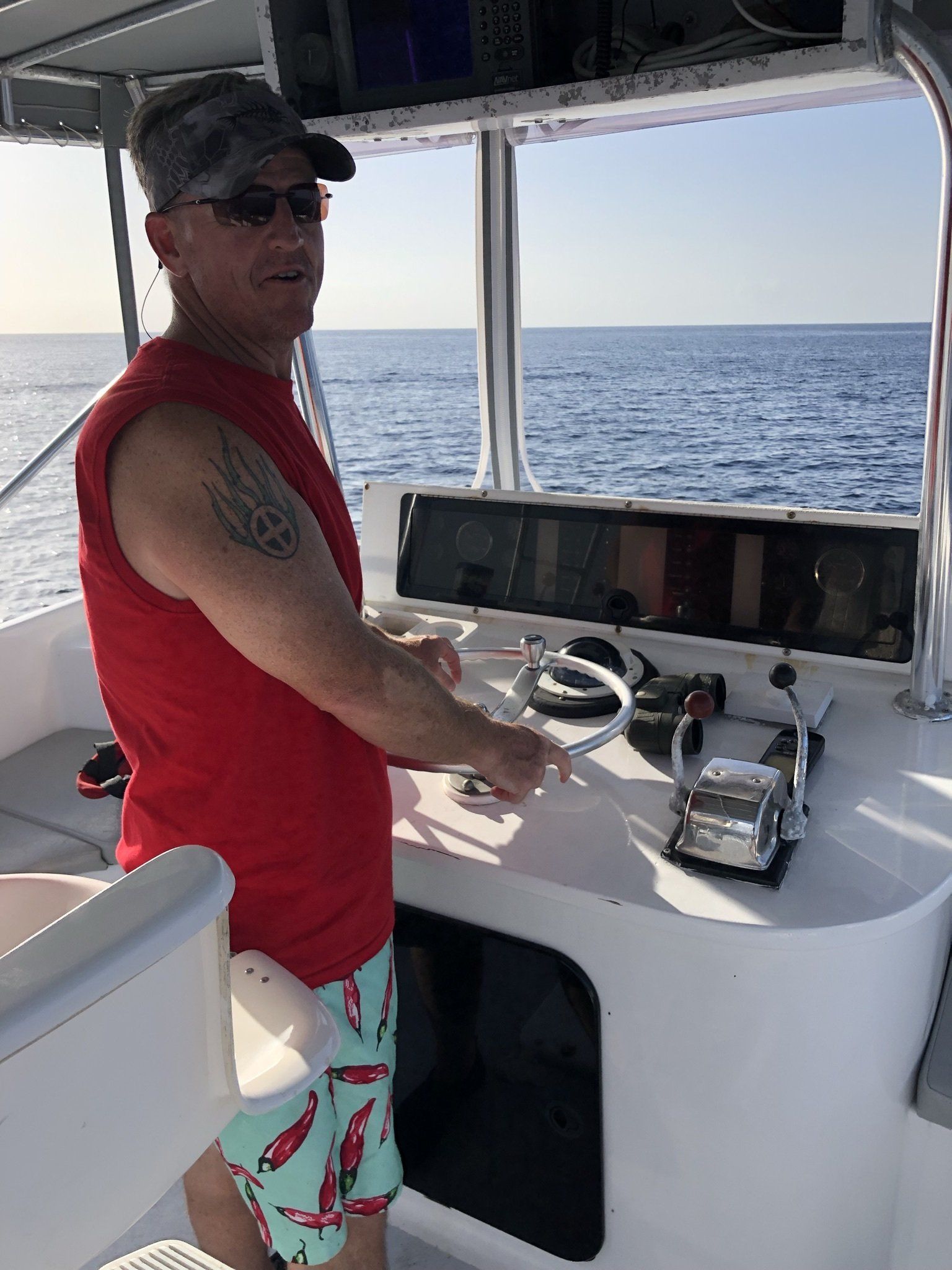 A man is sitting at the helm of a boat in the ocean.