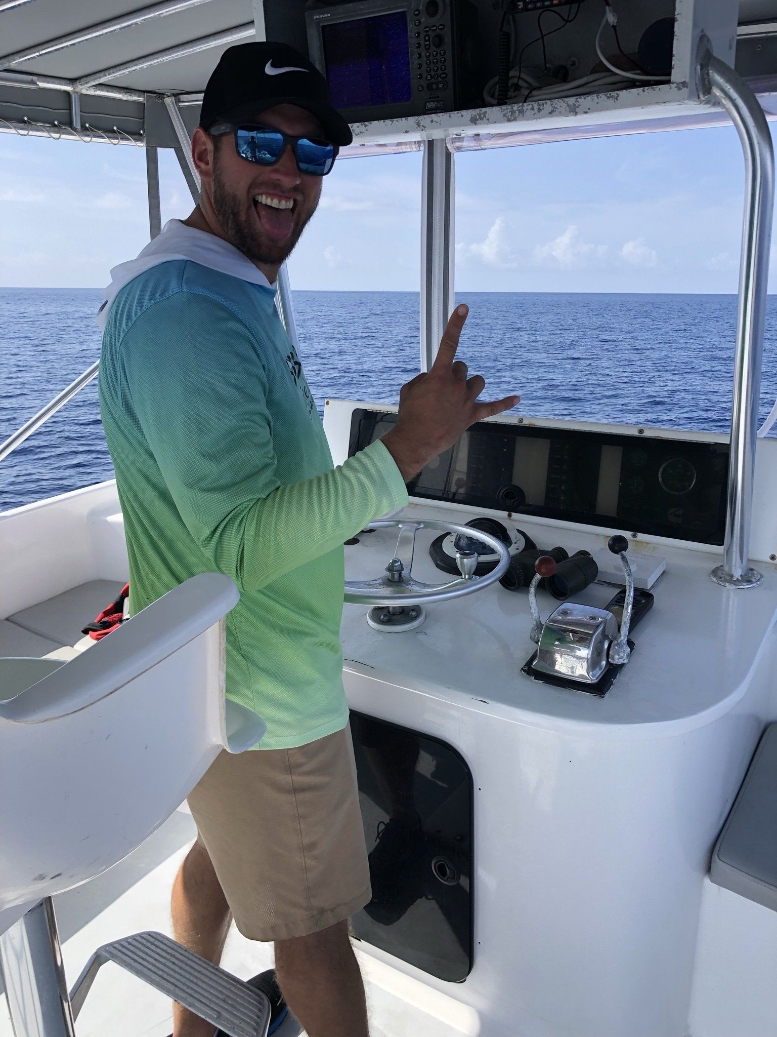 A man is standing at the helm of a boat in the ocean.