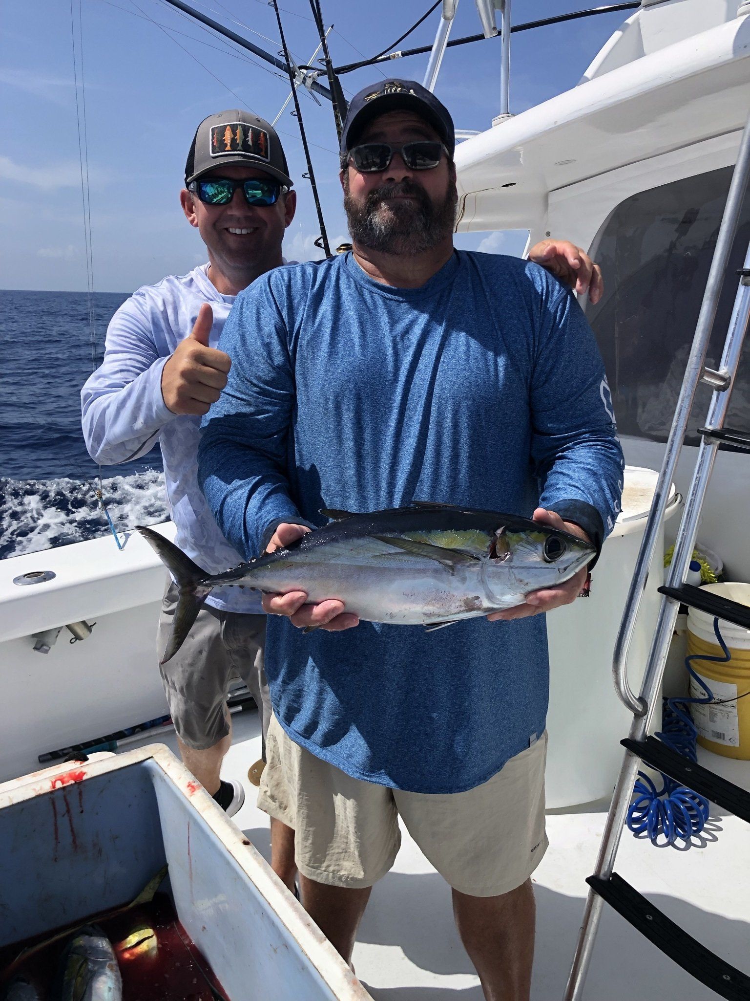 Two men are standing on a boat holding a fish and giving a thumbs up.
